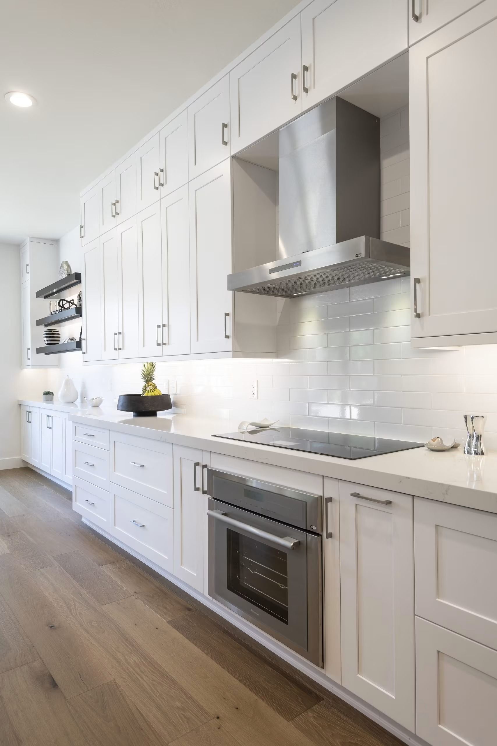 Bright white galley kitchen with stainless steel oven, range hood, and wood floors