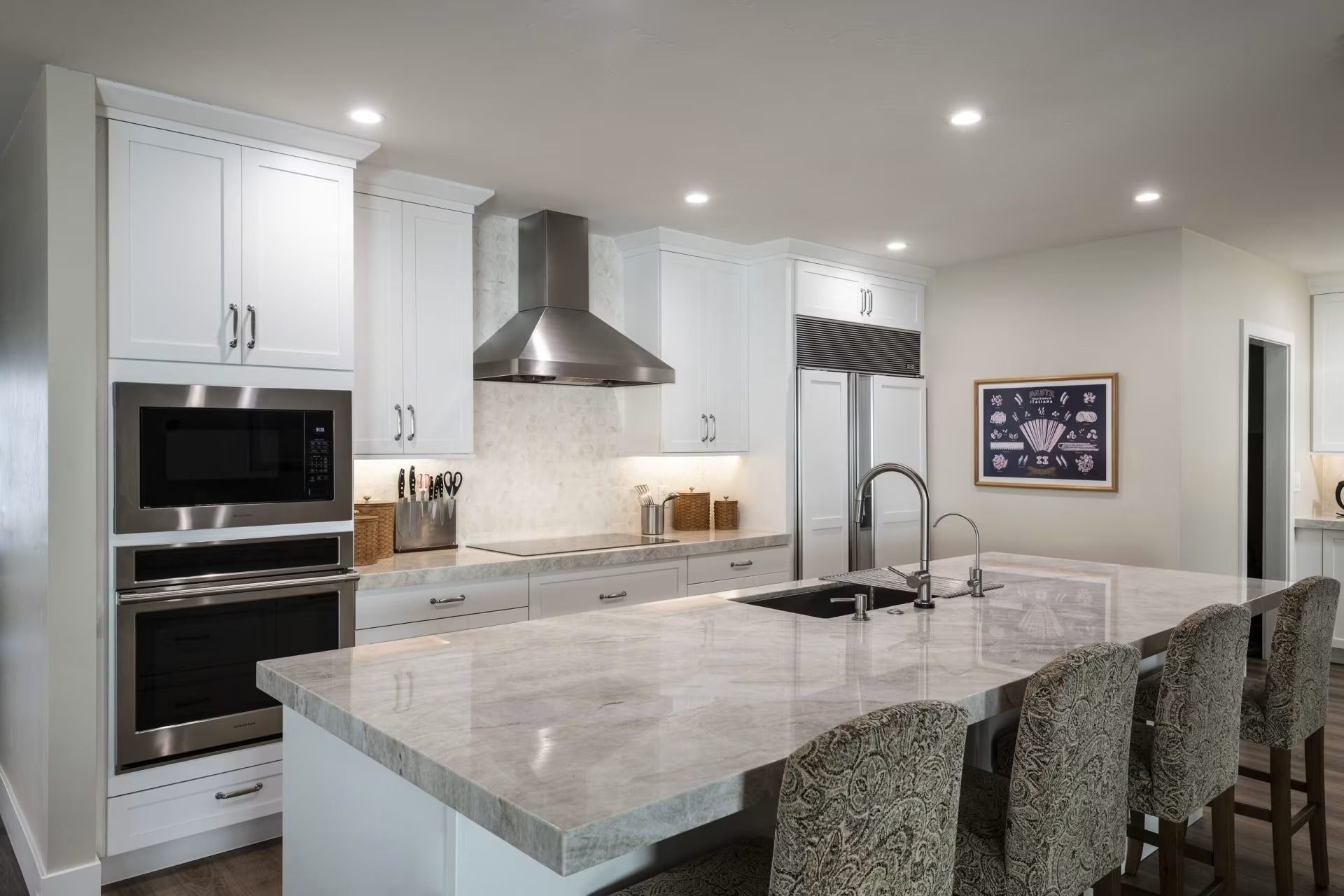 Modern white kitchen with marble island, stainless steel appliances, and patterned bar stools