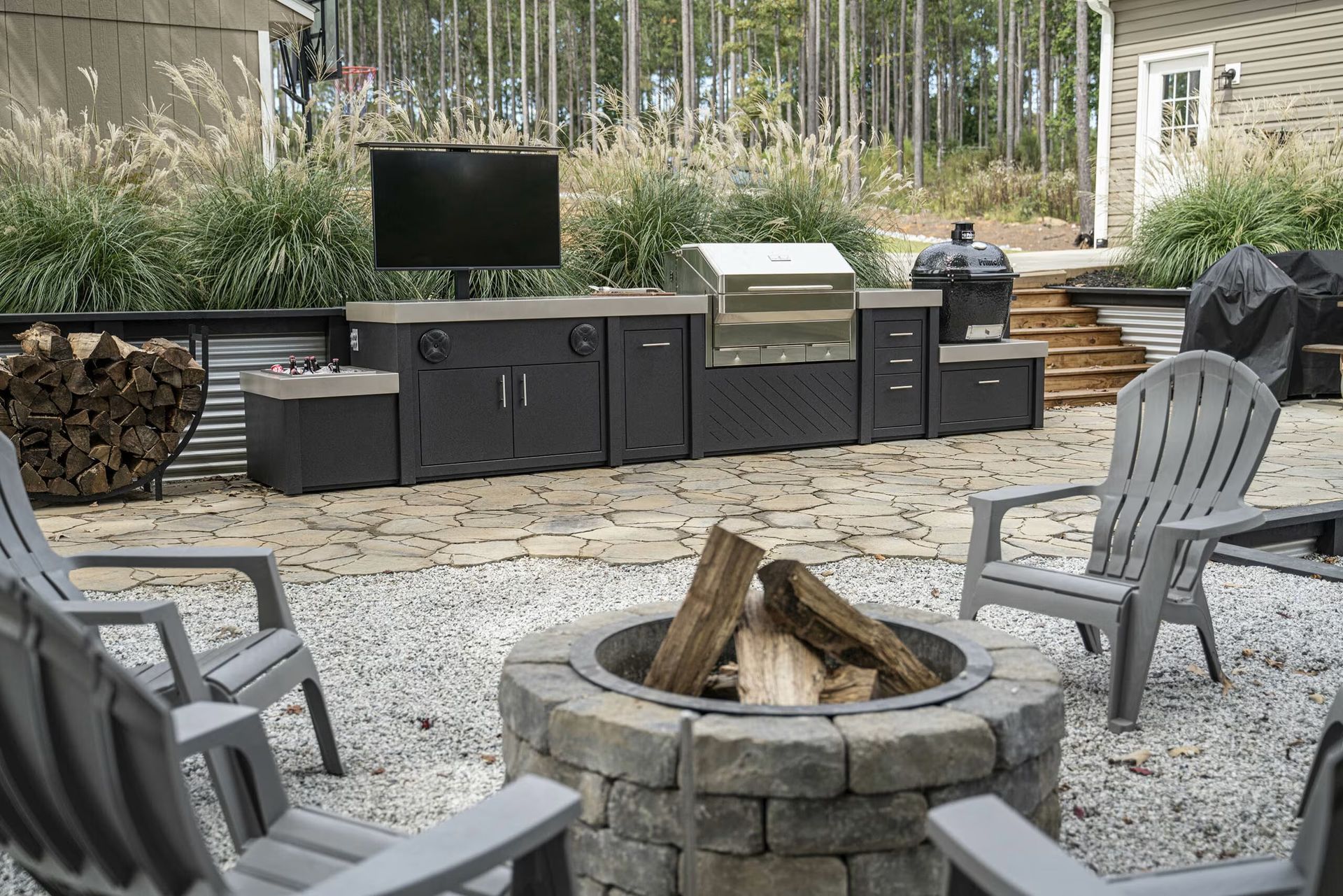 Backyard patio with fire pit, outdoor kitchen, grill, and chairs on gravel