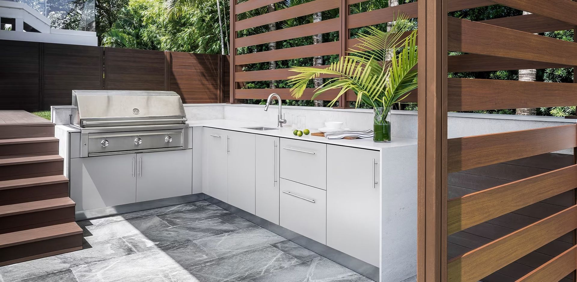 Modern outdoor patio kitchen with stainless steel grill, white cabinets, and wood privacy fencing