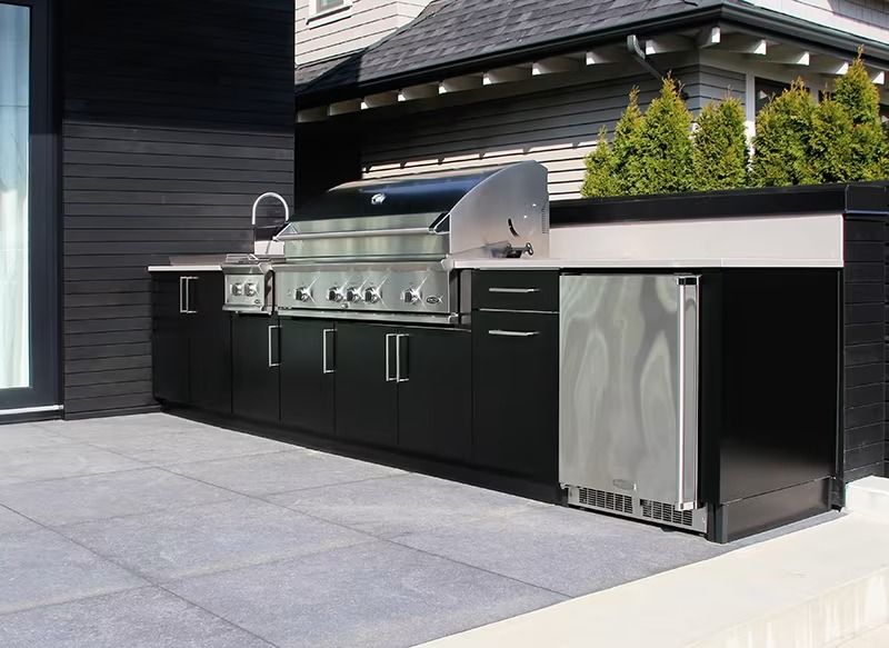 Outdoor built-in black grill and bar area with stainless steel appliances beside a modern house