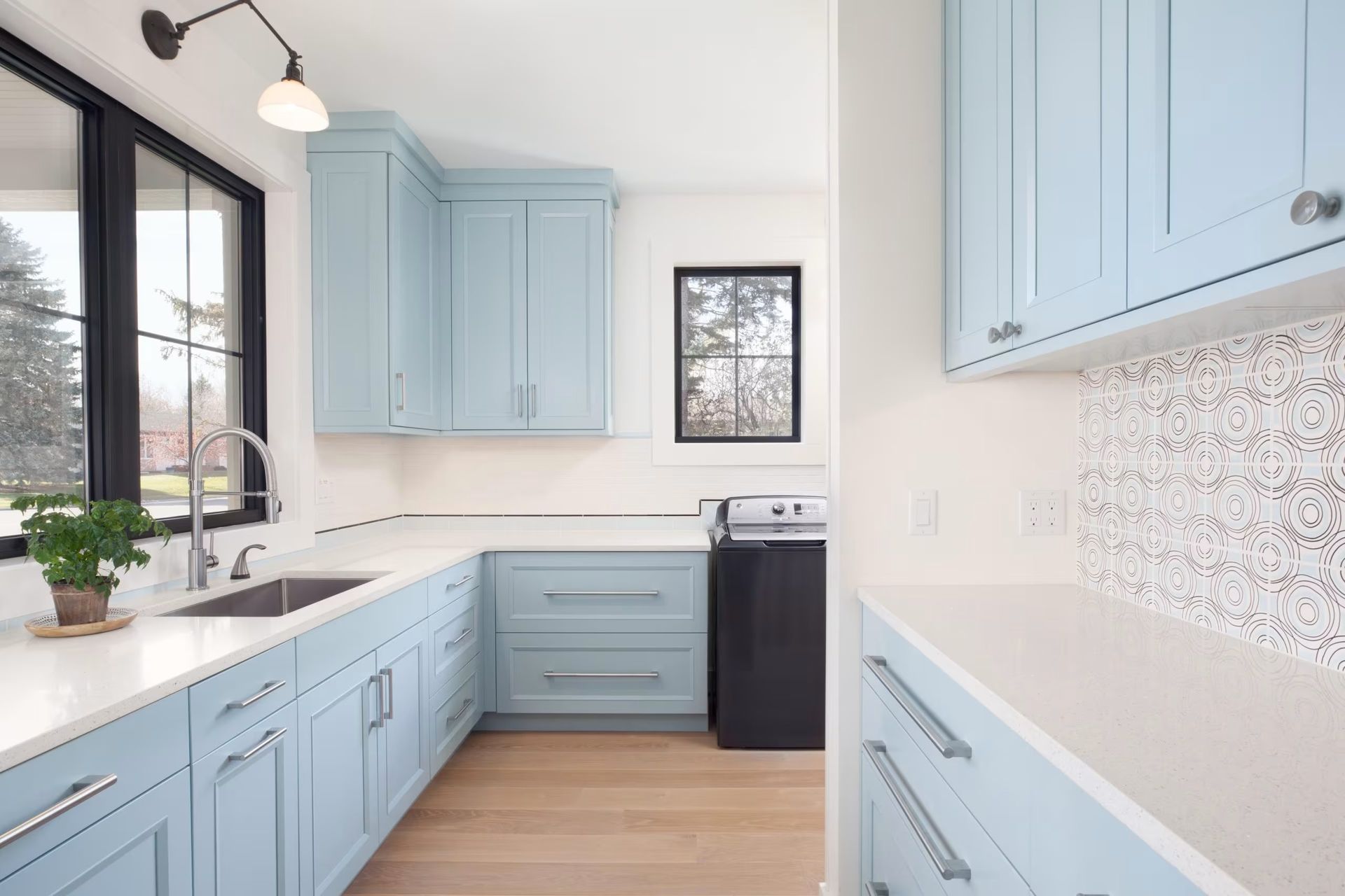 Bright kitchen with light blue cabinets, white counters, black oven, and large window