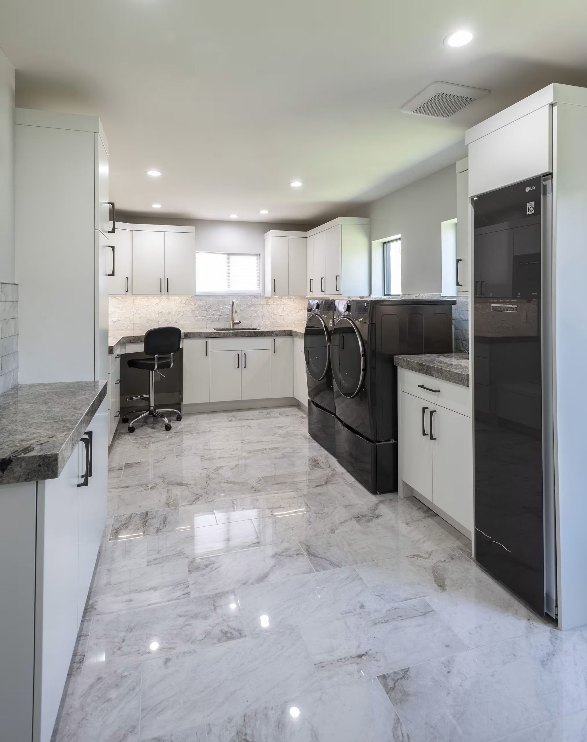 Modern white kitchen with marble floors, dark appliances, and granite countertops