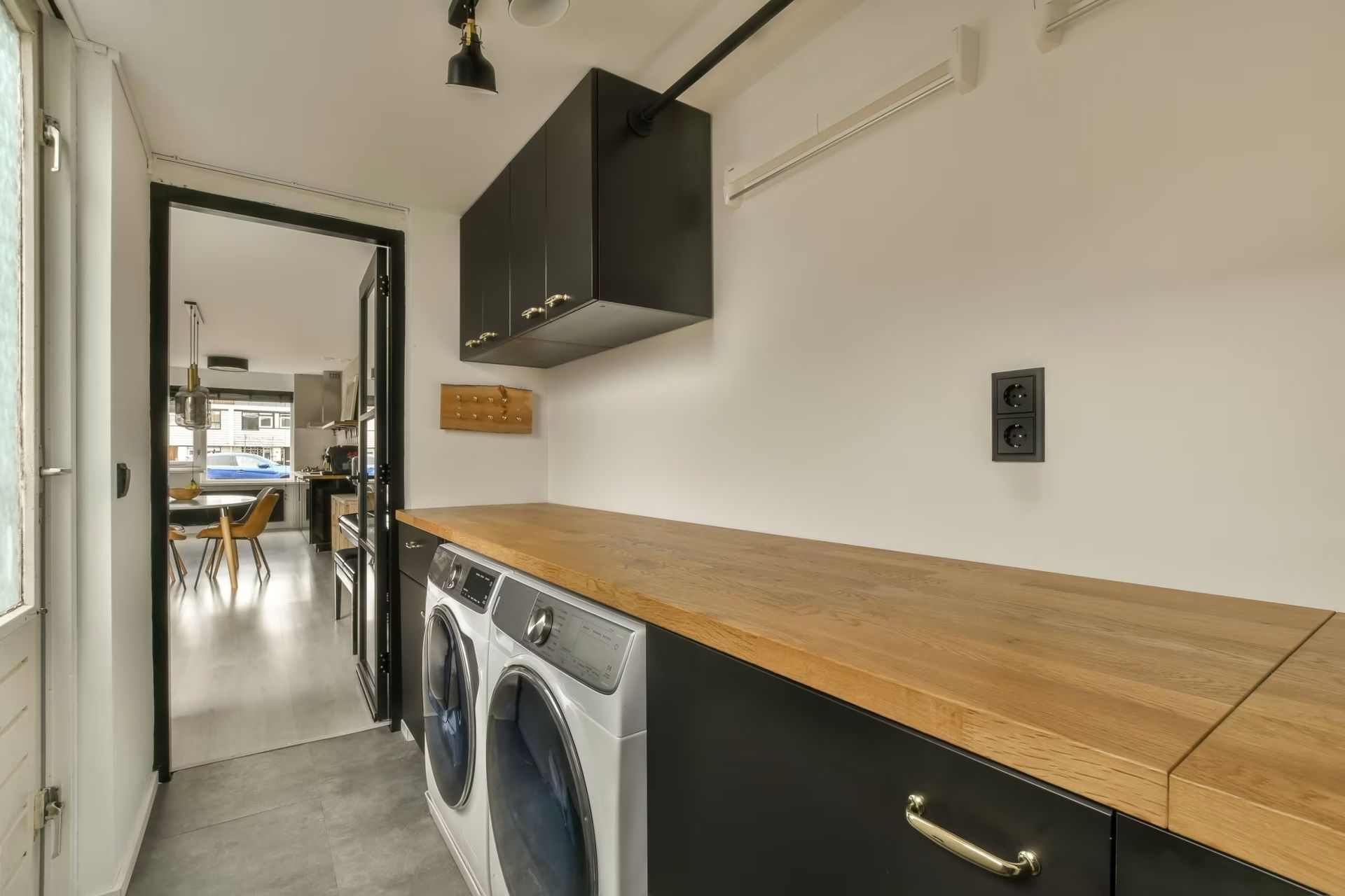 Laundry room with black cabinets, wooden countertop, and washer-dryer along a narrow hallway
