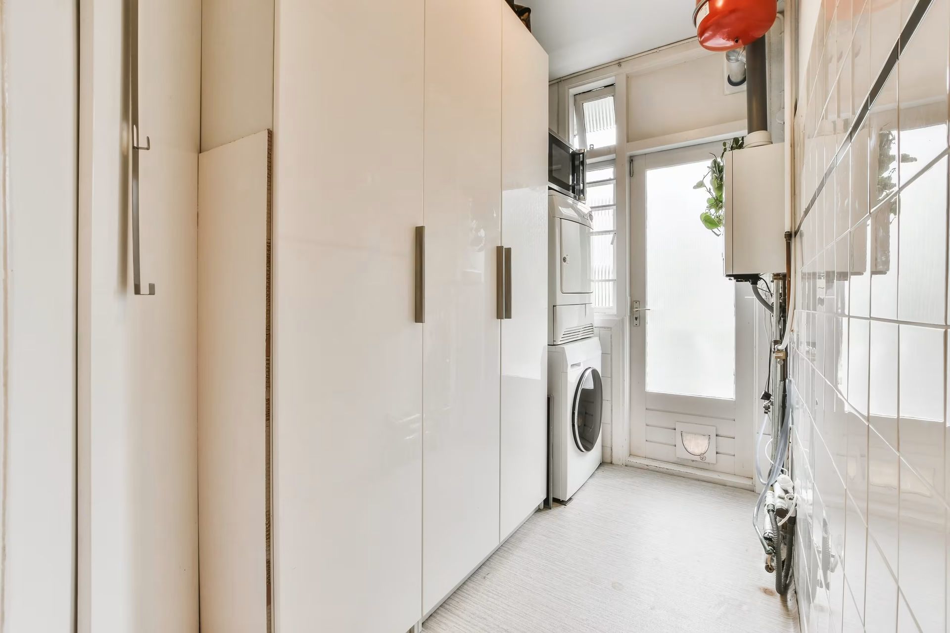 Narrow white hallway with built-in cabinets, tiled walls, and a door at the end.