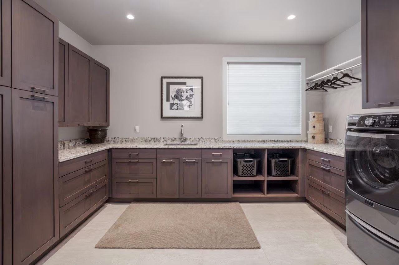 Modern kitchen with dark cabinets, white countertops, stainless appliances, and a window over the sink
