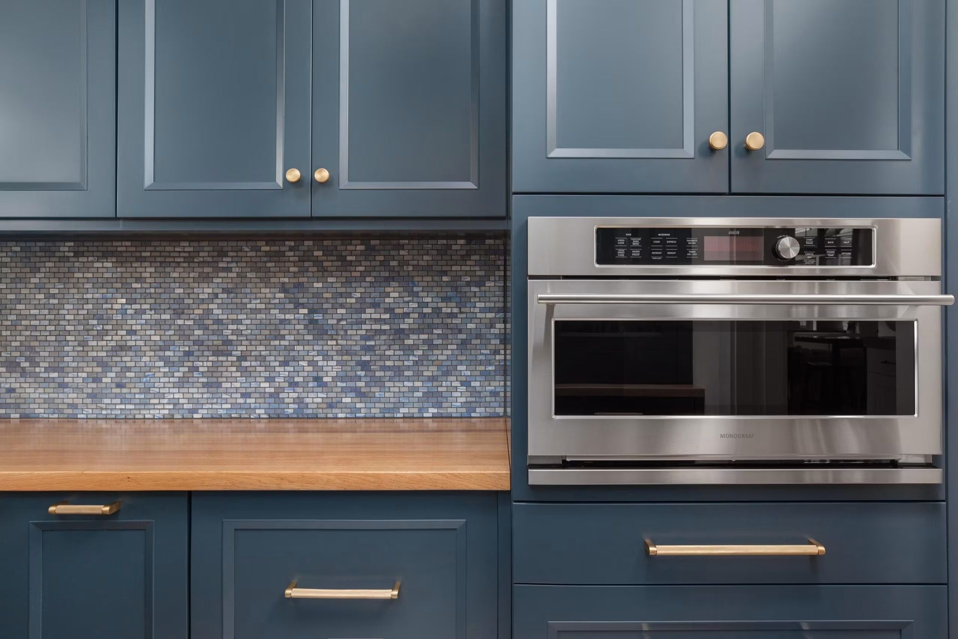 Blue kitchen cabinets with wood countertop and stainless steel oven, plus mosaic tile backsplash.