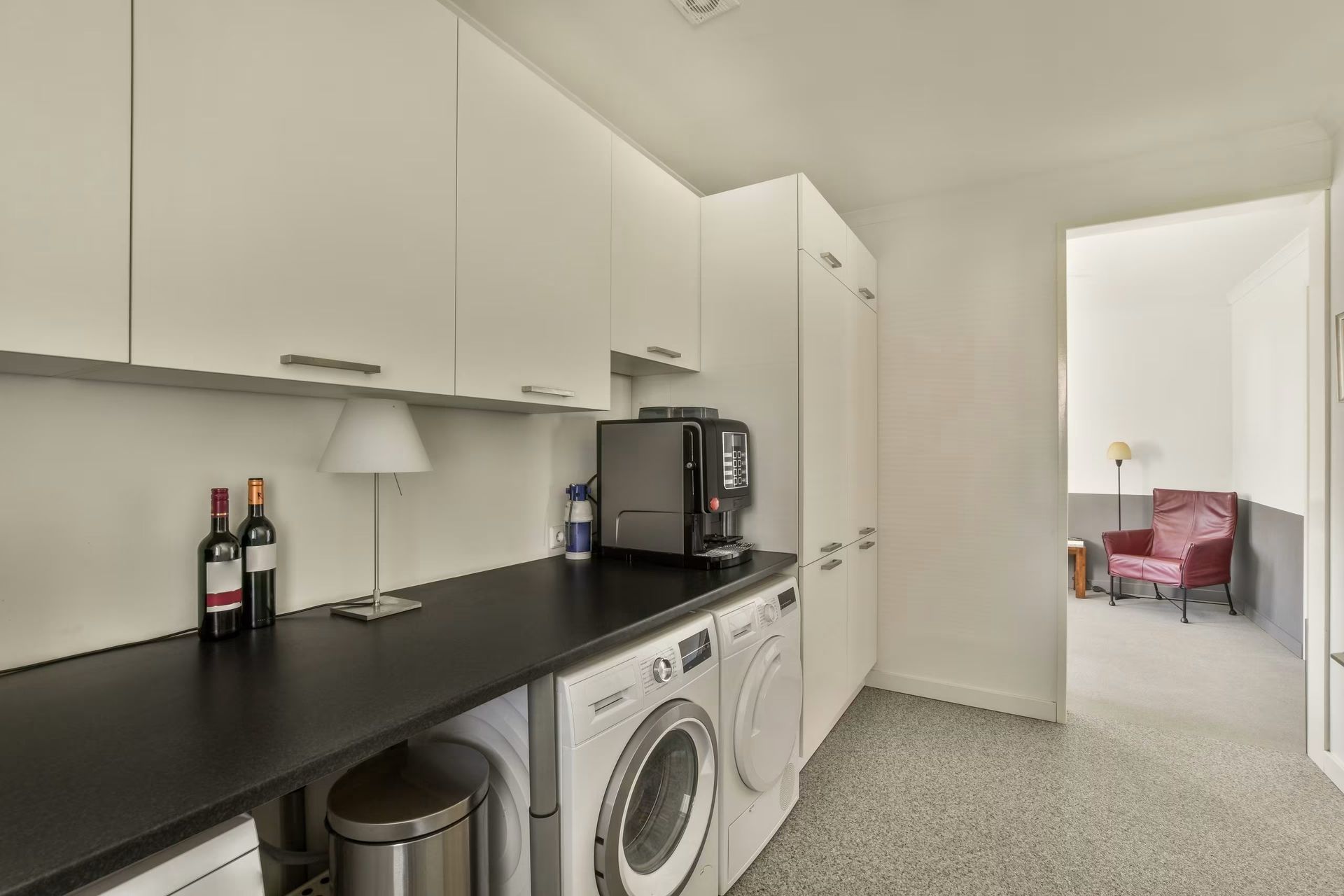 Bright kitchen with white cabinets, black countertop, washer, dryer, and coffee machine; doorway to pink living room