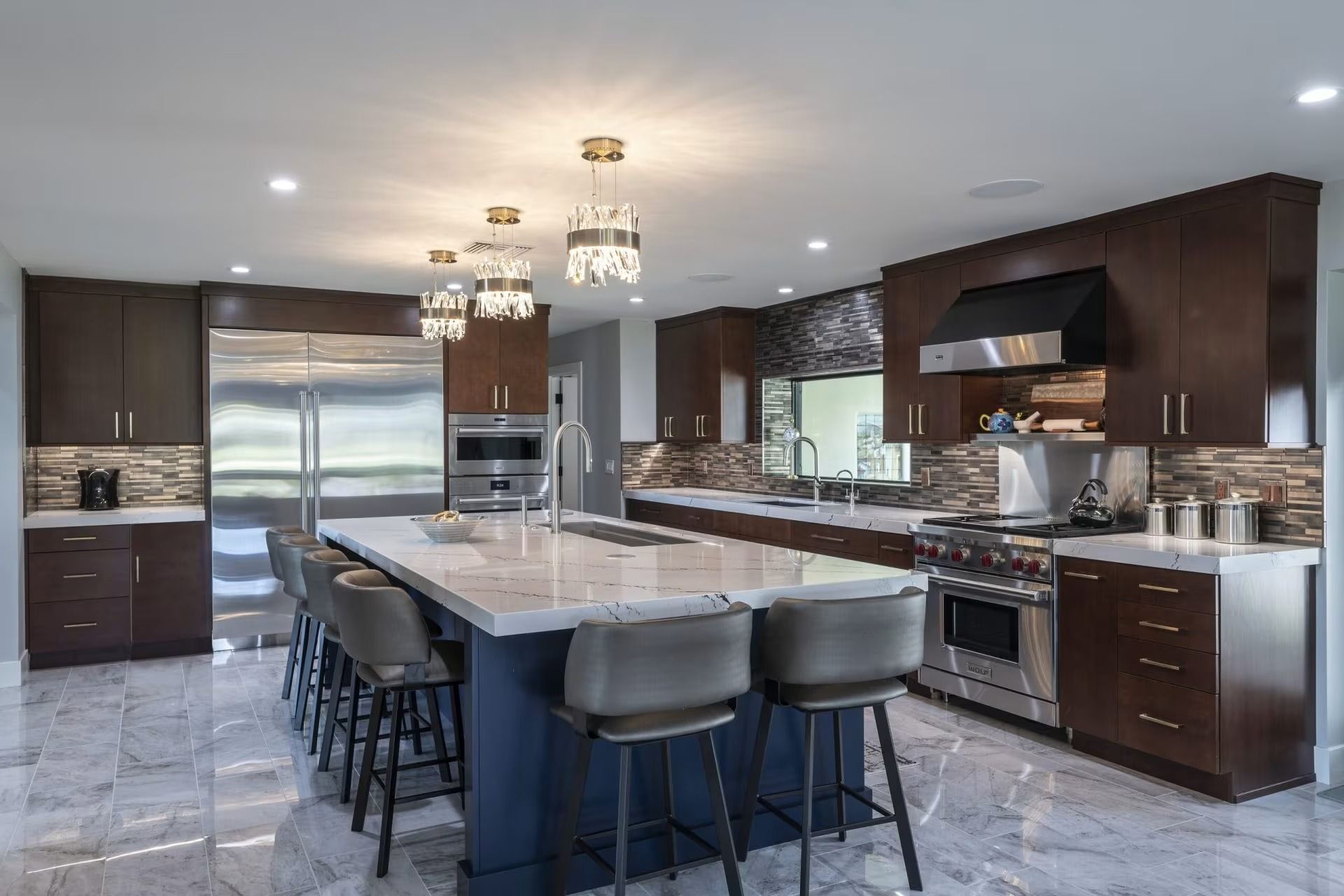 Modern kitchen with dark cabinets, stainless steel appliances, and a large marble island with bar stools