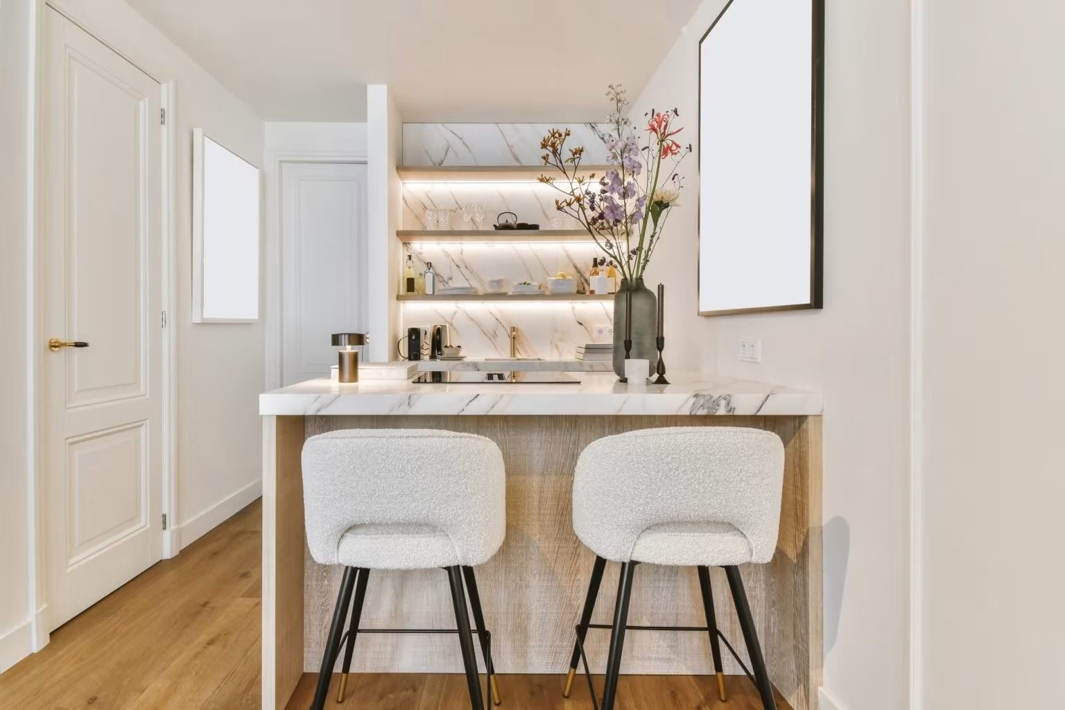 Bright modern kitchen with marble island, two white stools, and open shelves with decor