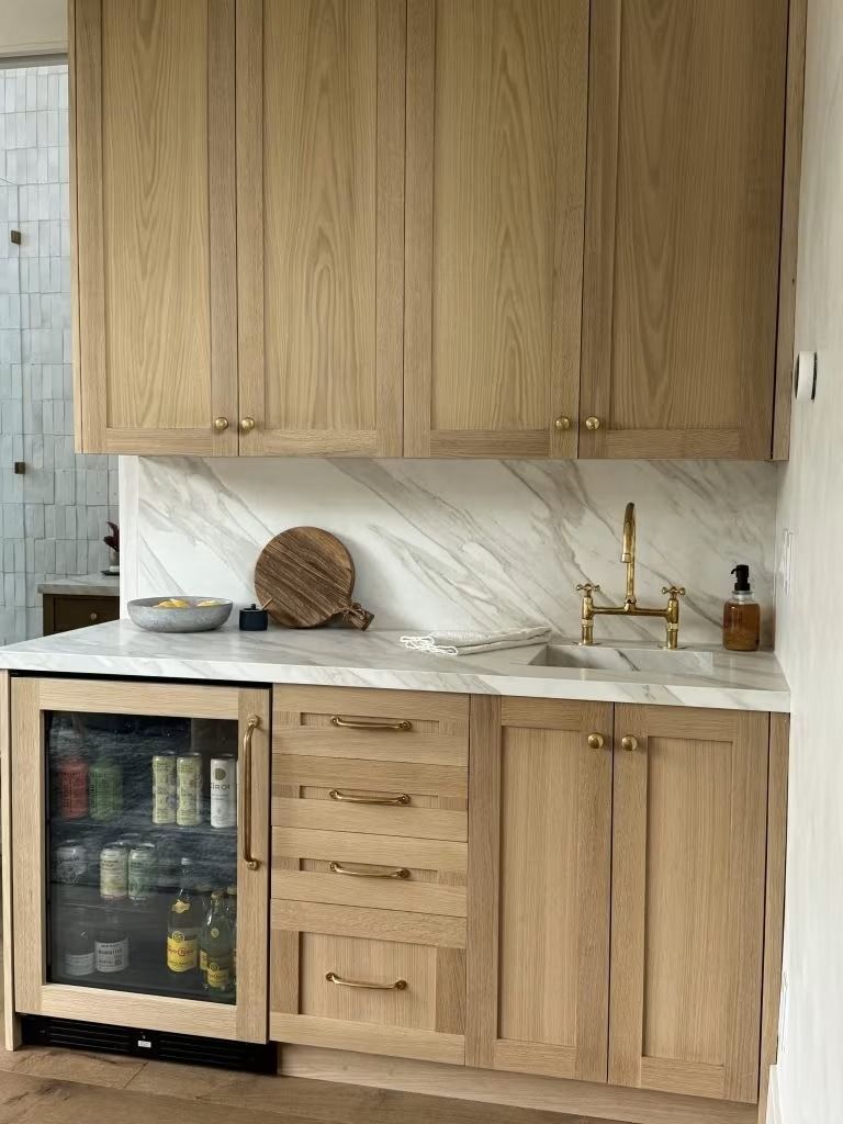 Wooden kitchen cabinets, marble backsplash, and countertop with a small sink and wine fridge beneath.