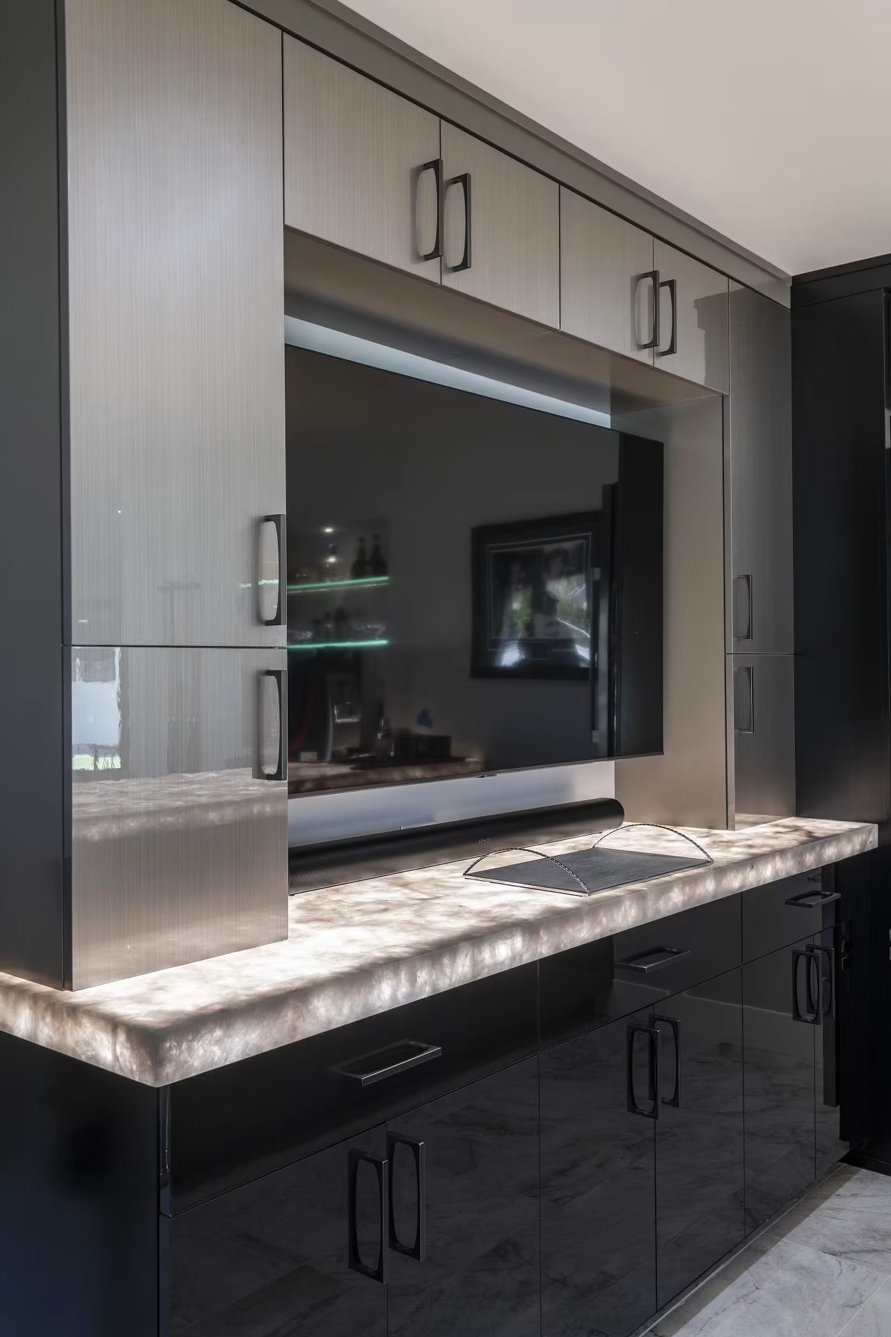 Built-in TV cabinet with light wood and black lower cabinets, marble countertop, and wall-mounted TV.