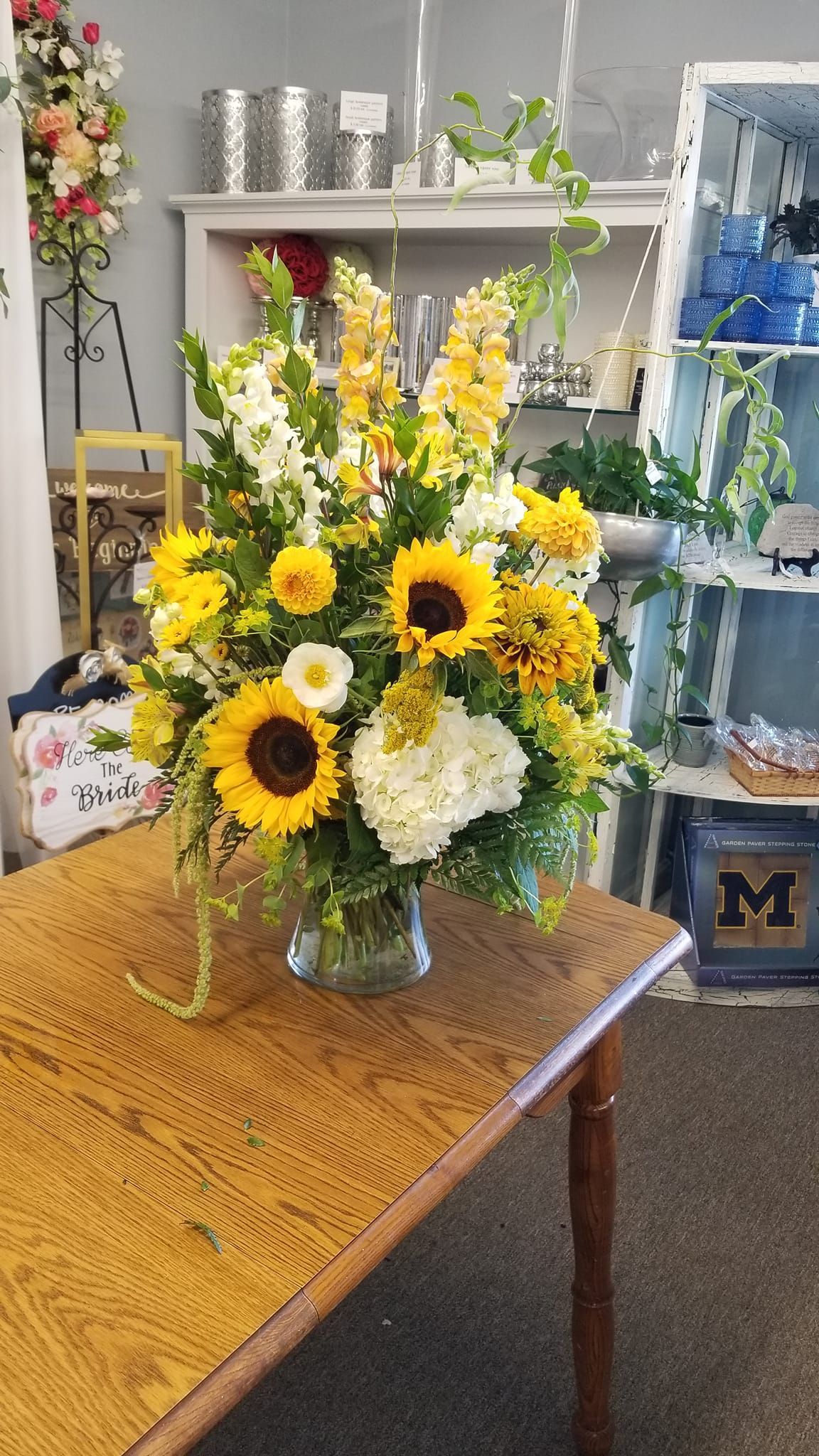 A vase filled with yellow and white flowers is sitting on a wooden table.