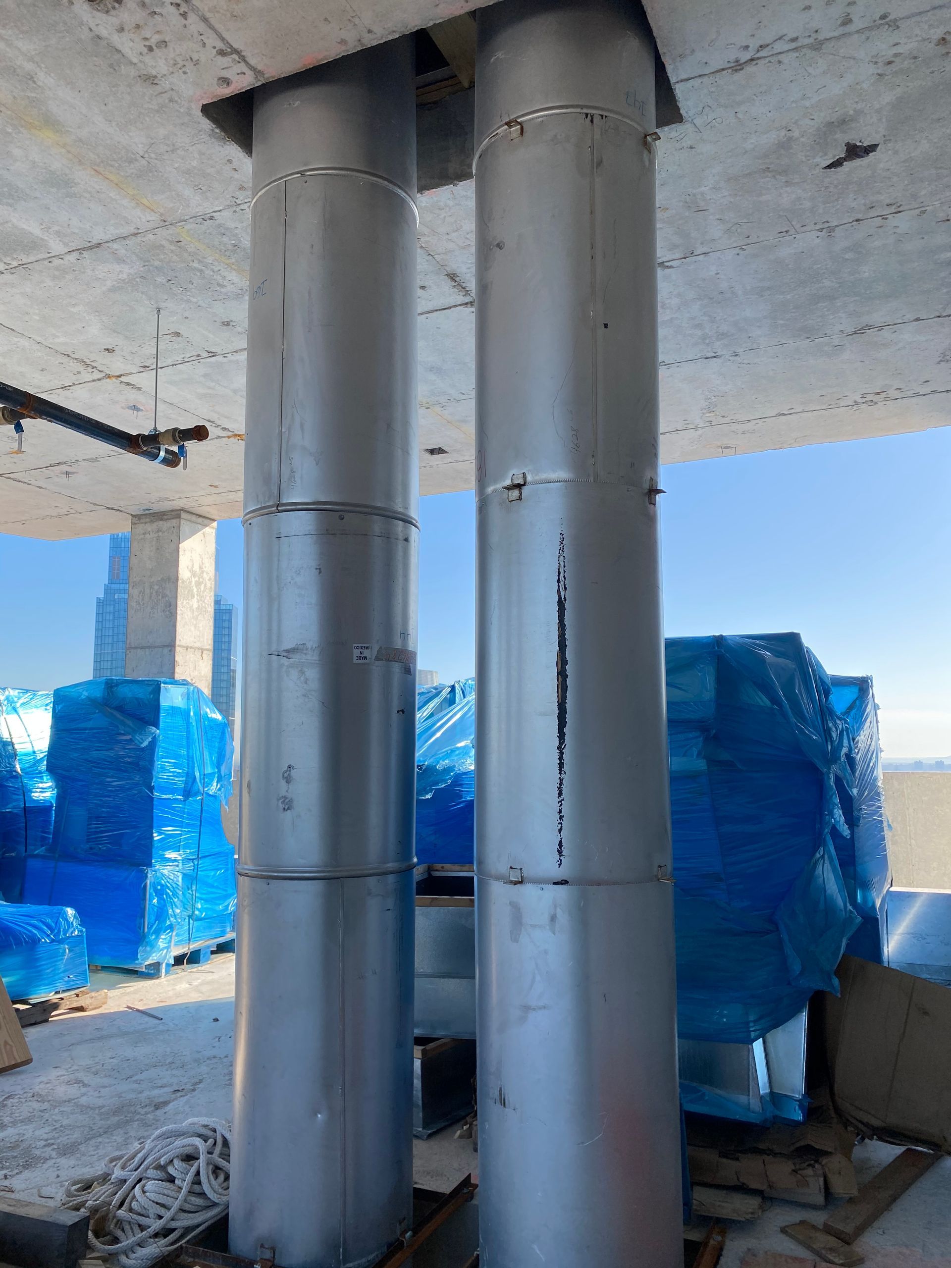 Two large metal columns support a concrete ceiling, construction site setting.