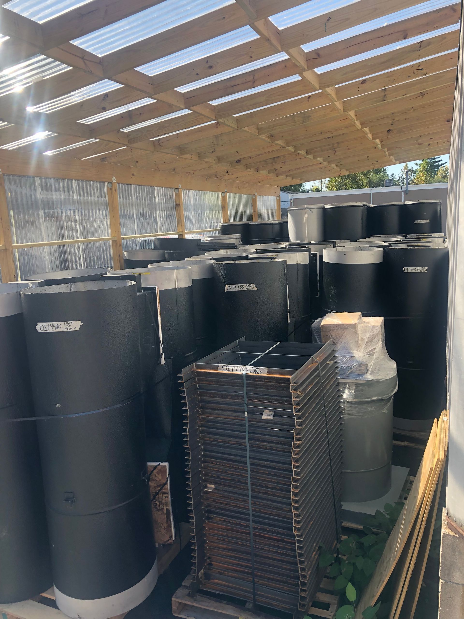 Large black water tanks stored under a wooden and corrugated plastic shelter.