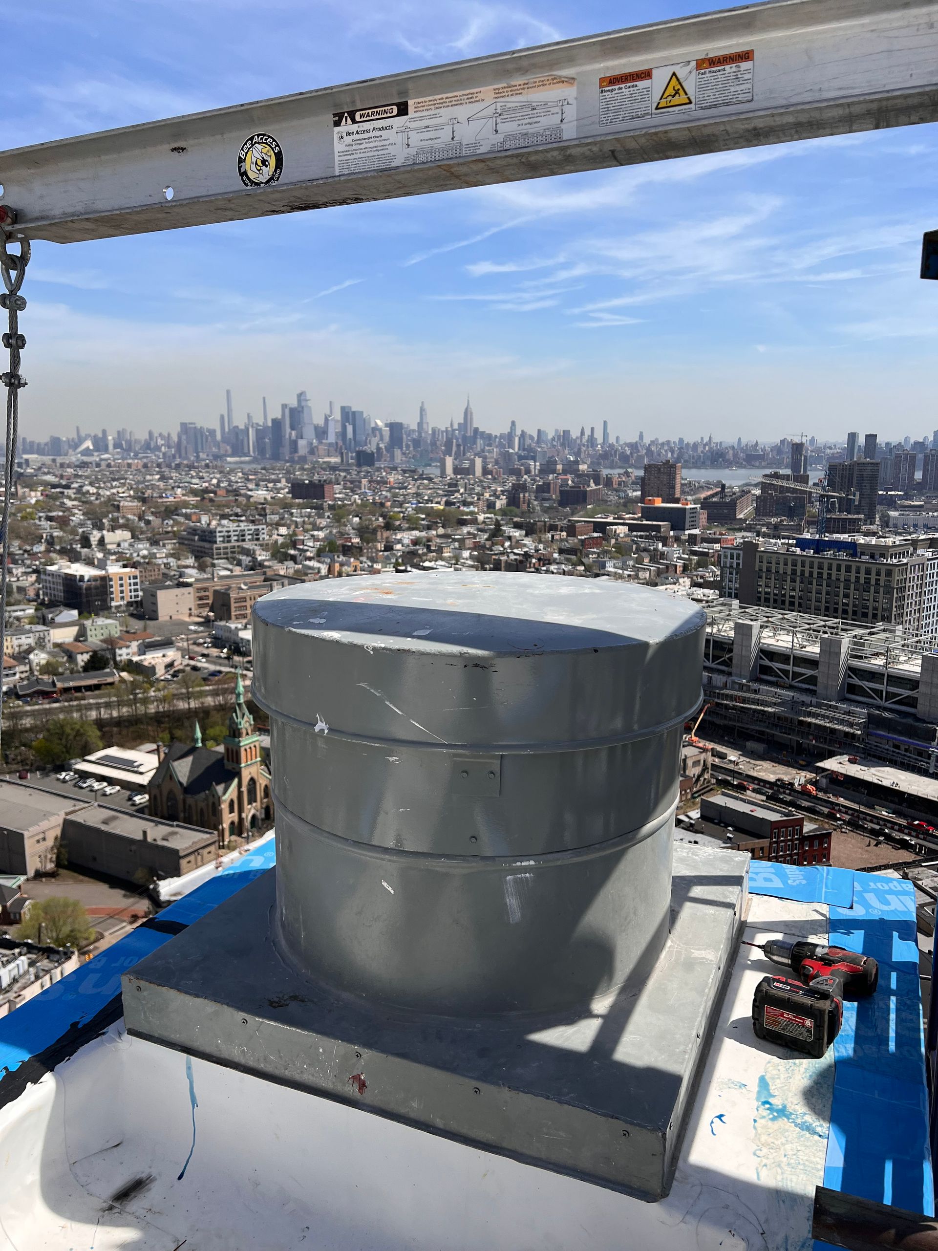 Metal ventilation unit on a rooftop with a city skyline in the background on a sunny day.