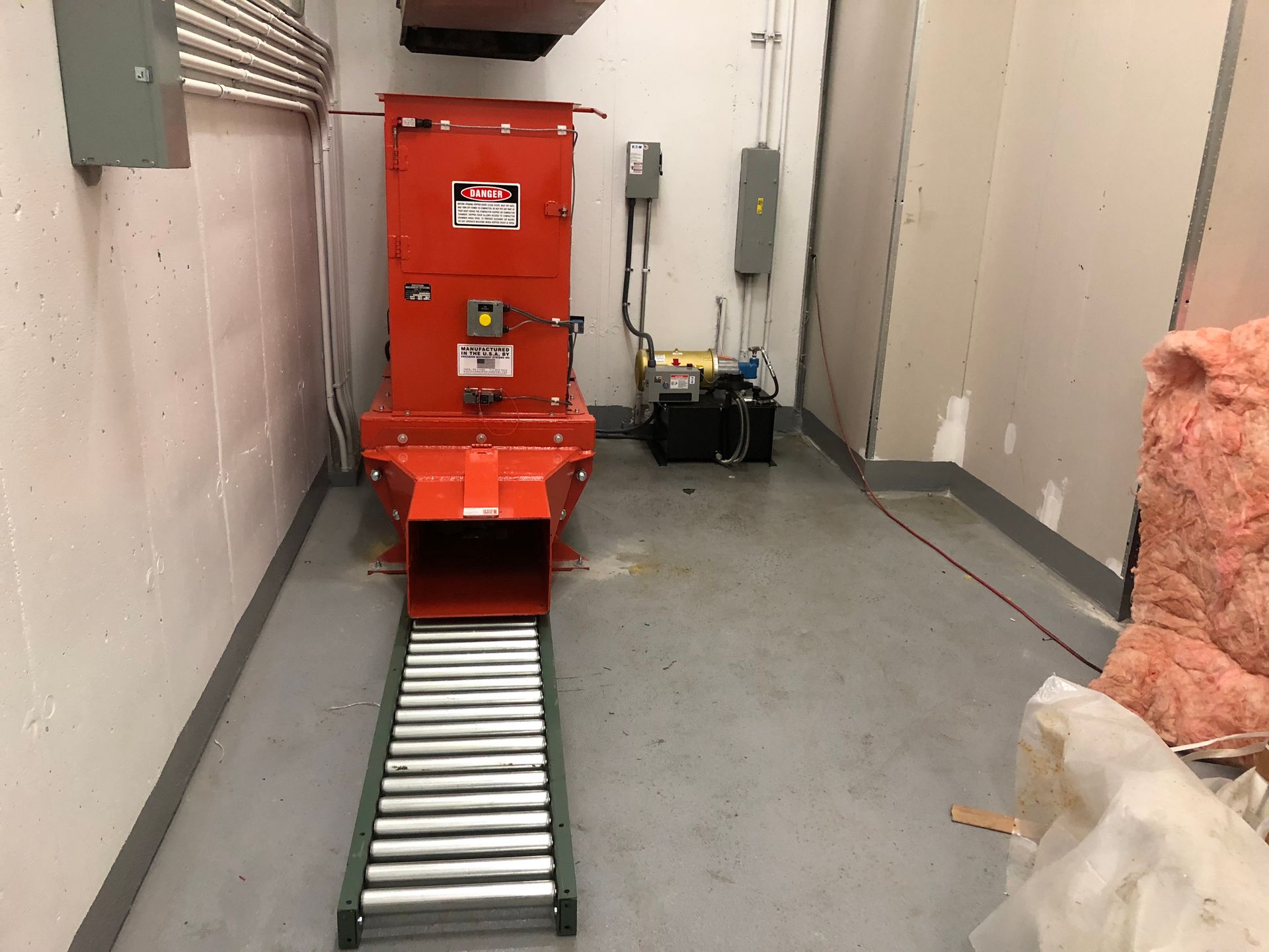 Orange industrial shredder with conveyor belt in a room.
