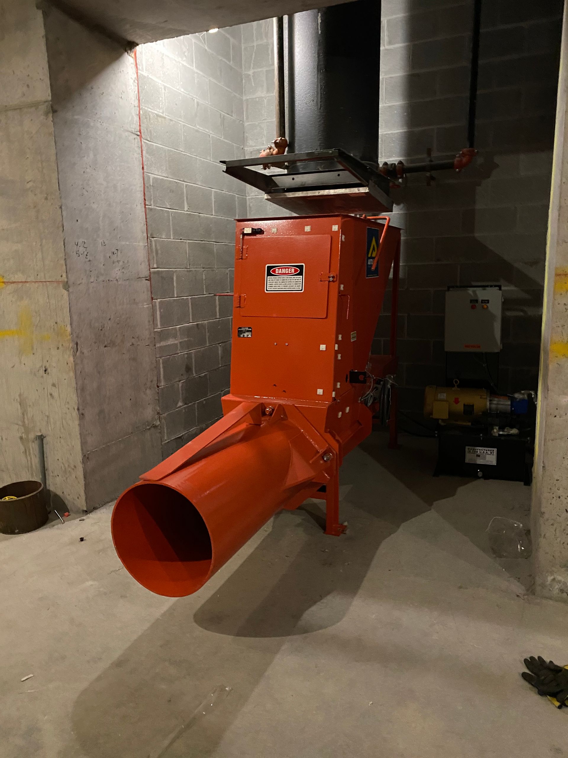 Large, red industrial machine in a concrete room; looks like a blower or shredder.