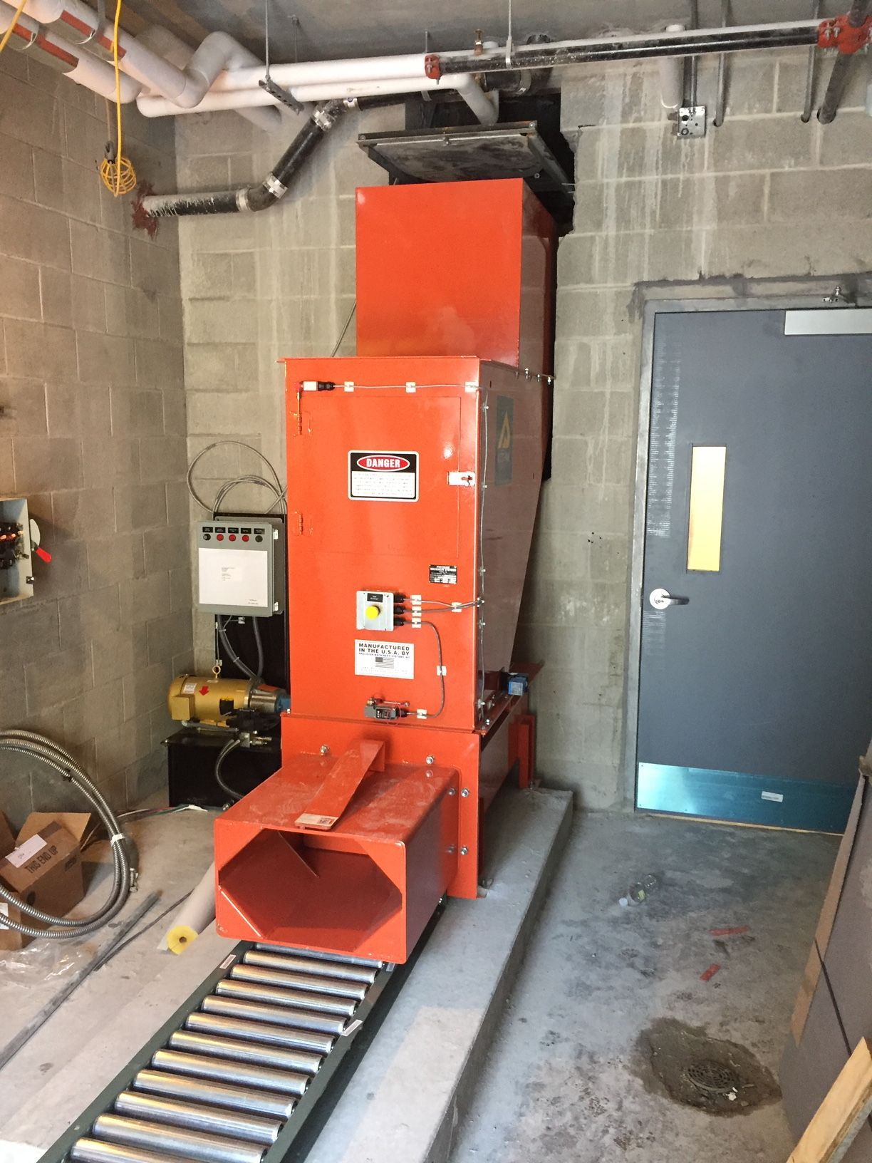 Orange construction waste chute in a concrete room with a door.