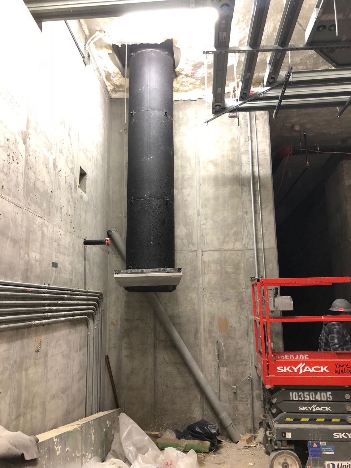 Black ductwork suspended in a concrete tunnel. A lift and piping are also visible.