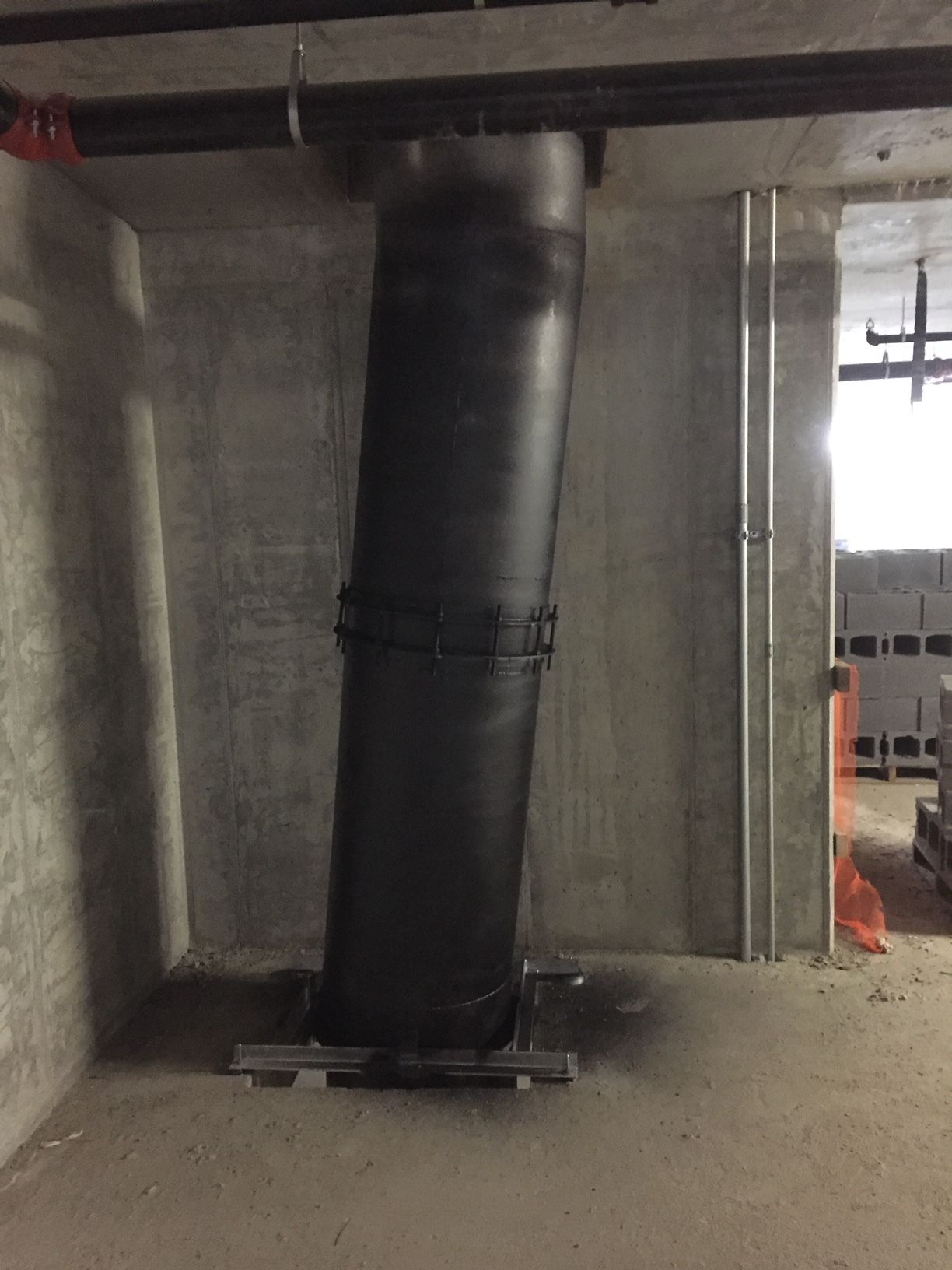Black cylindrical ducting through a concrete wall, held in place by metal brackets.
