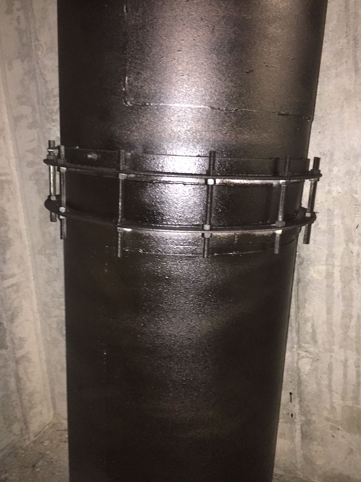 Black painted pipe section with a metal bracket around it.