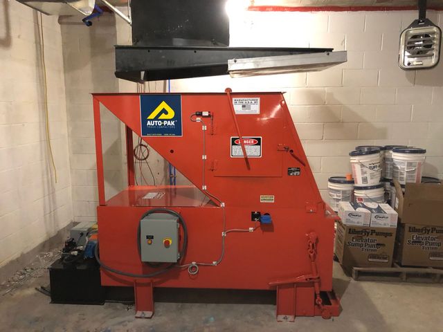 Red industrial machine with a control panel and warning signs, indoors.