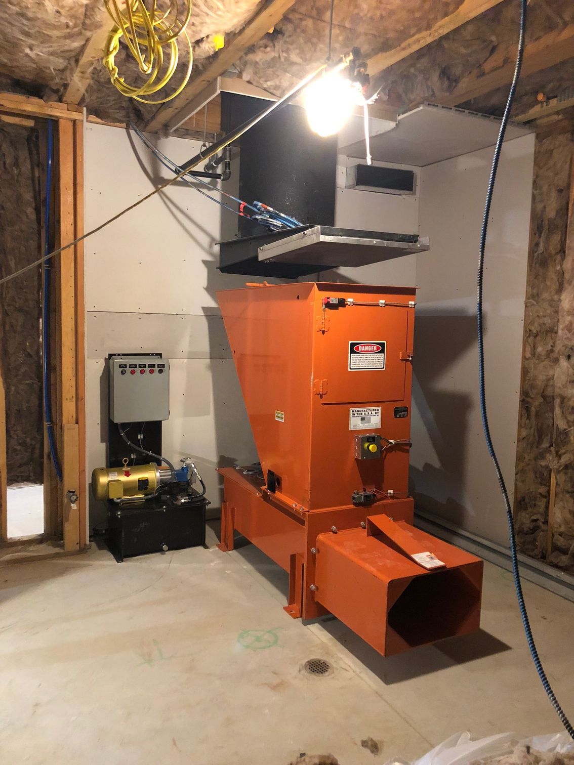 Orange industrial machine in a basement with electrical components and a light.