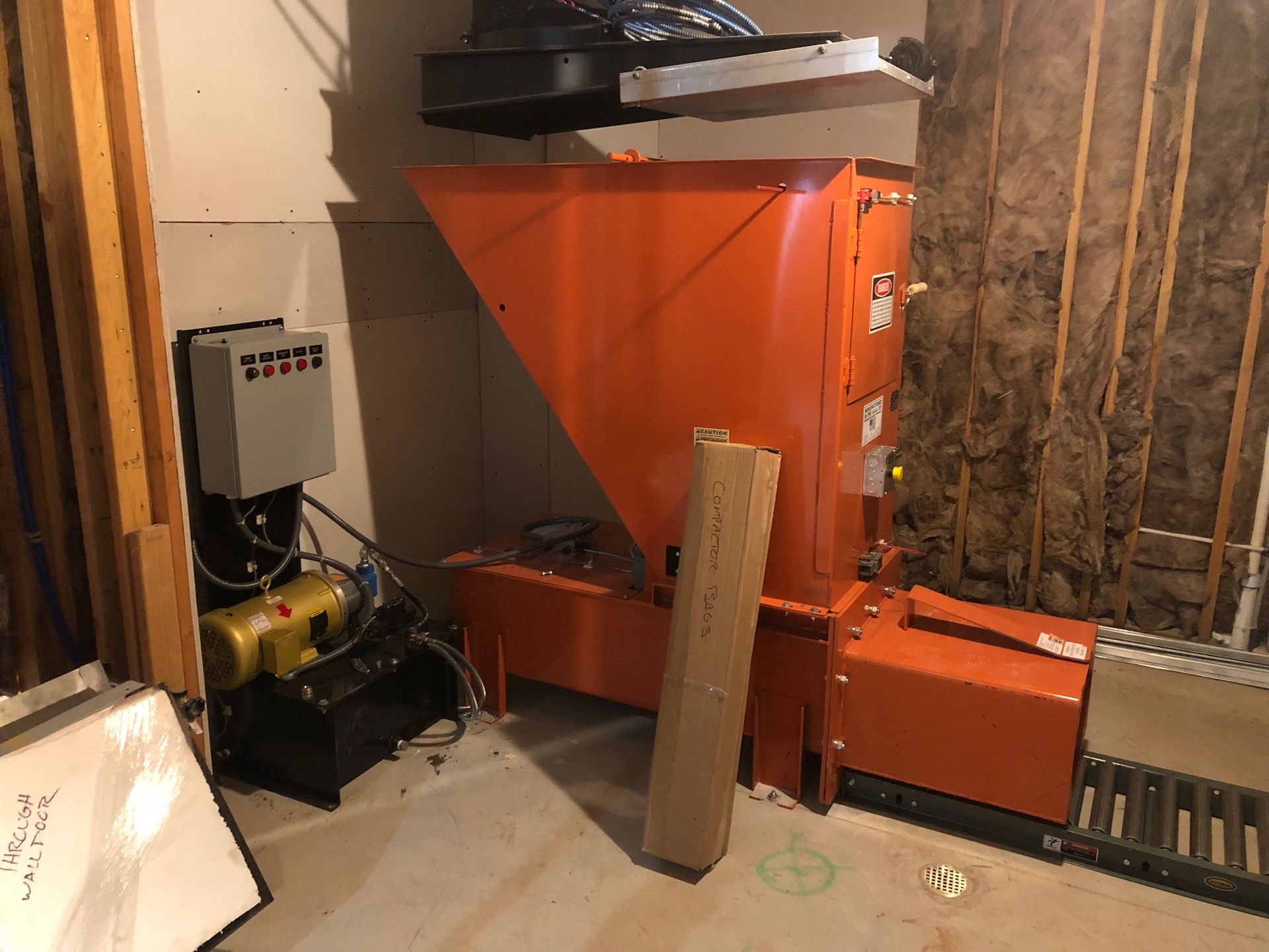 Orange industrial machine in a basement setting with electrical panel and supports.