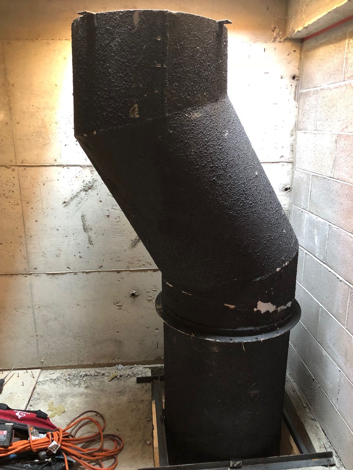 Black industrial ventilation pipe angled against a concrete wall in a basement.