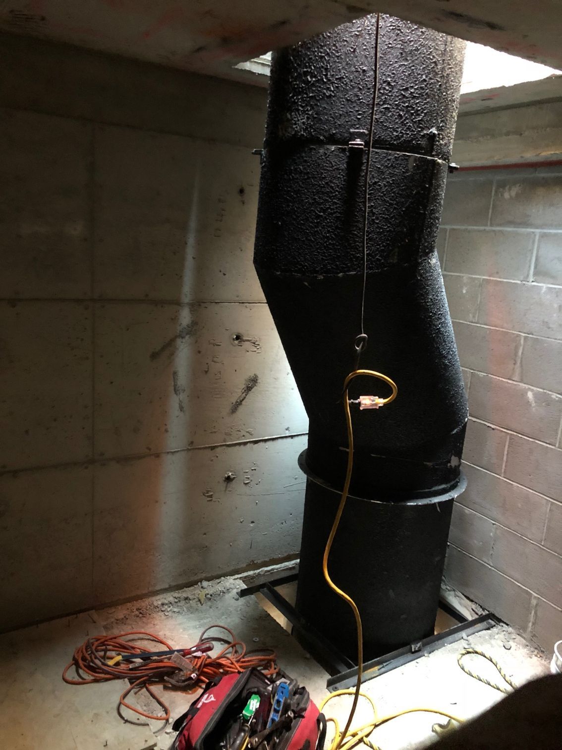 Black, curved pipe in a concrete enclosure; power cord and tools in the foreground.