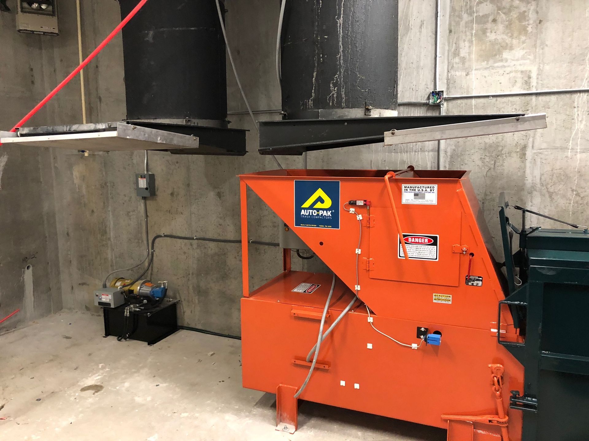 Orange industrial machine in a concrete room with two black vents overhead.