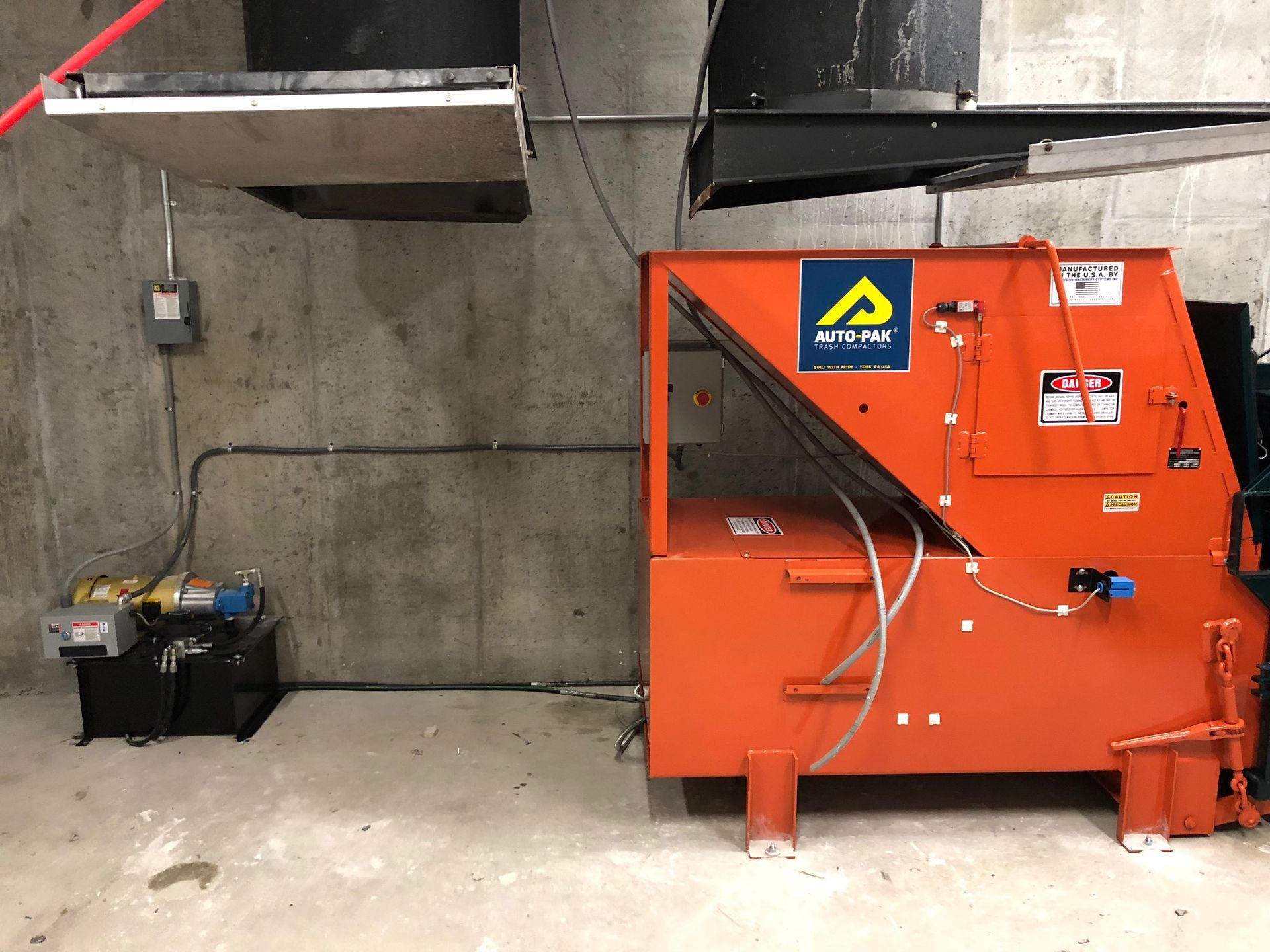 Orange industrial machine and hydraulic pump against a concrete wall.