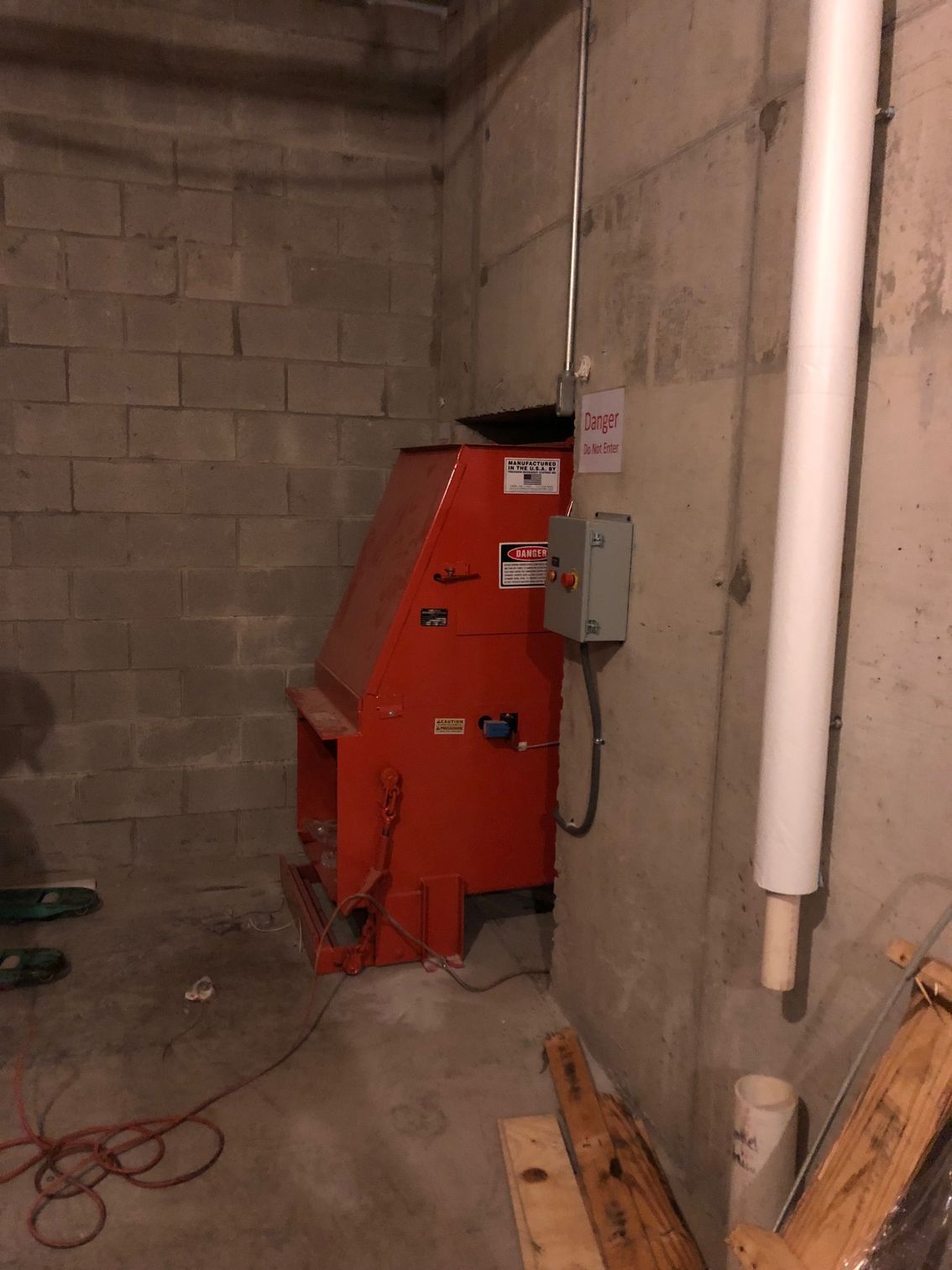 Red industrial machine in a concrete basement with electrical panel and pipes.