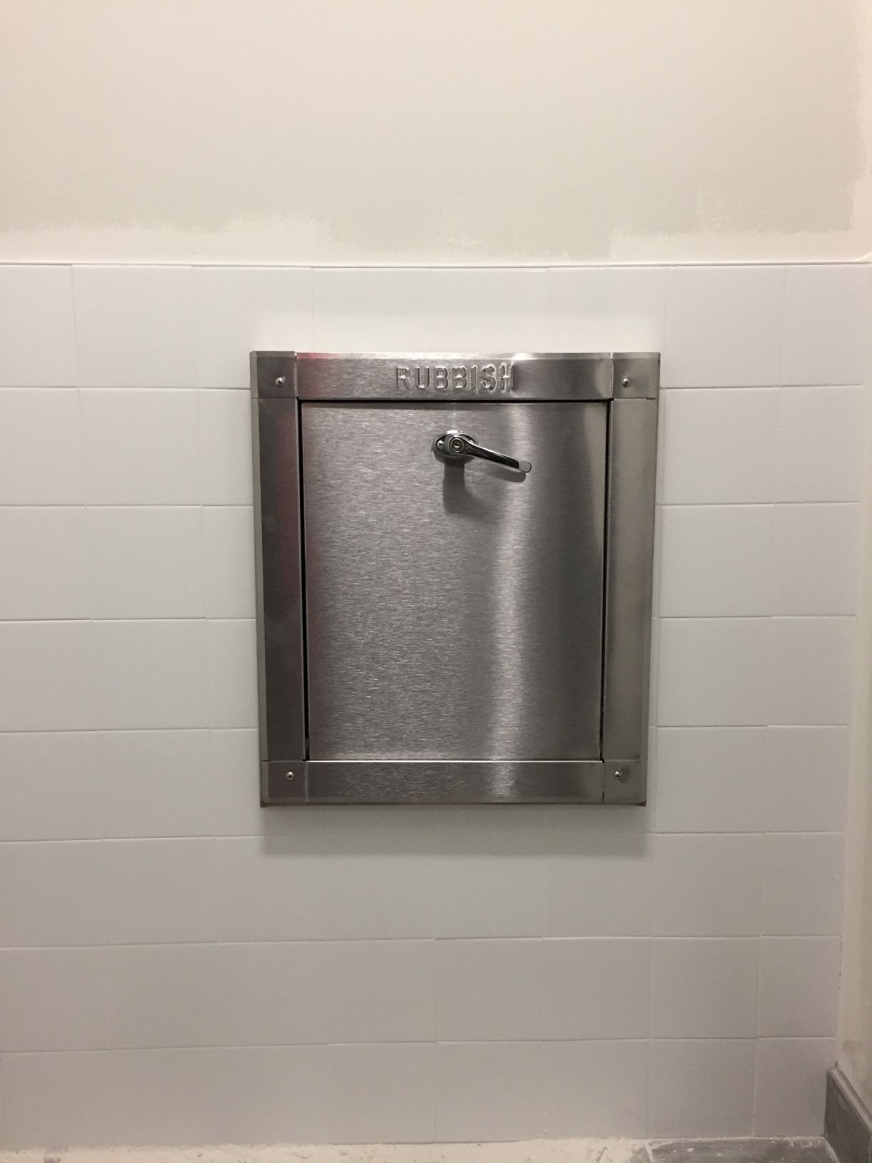 Stainless steel recessed fire hose cabinet on white tiled wall.