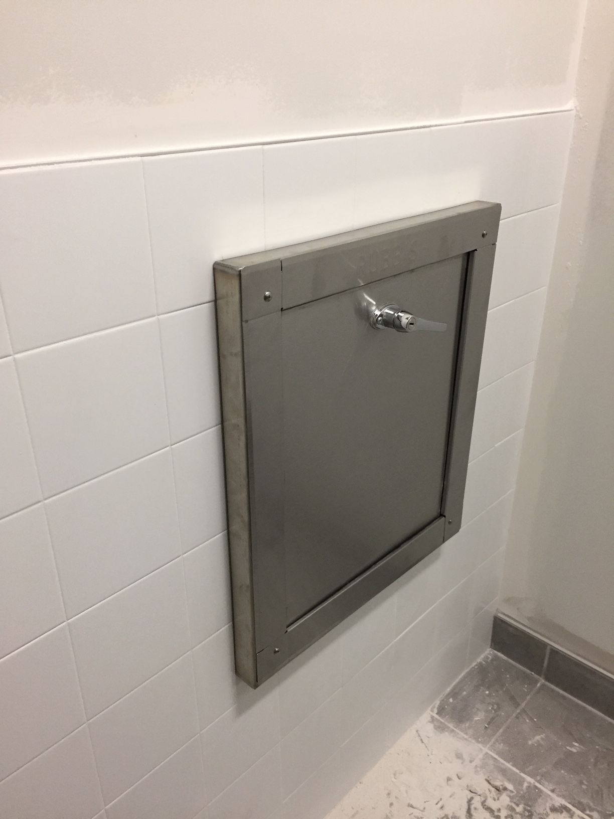 A stainless steel wall-mounted trash chute on a tiled wall.