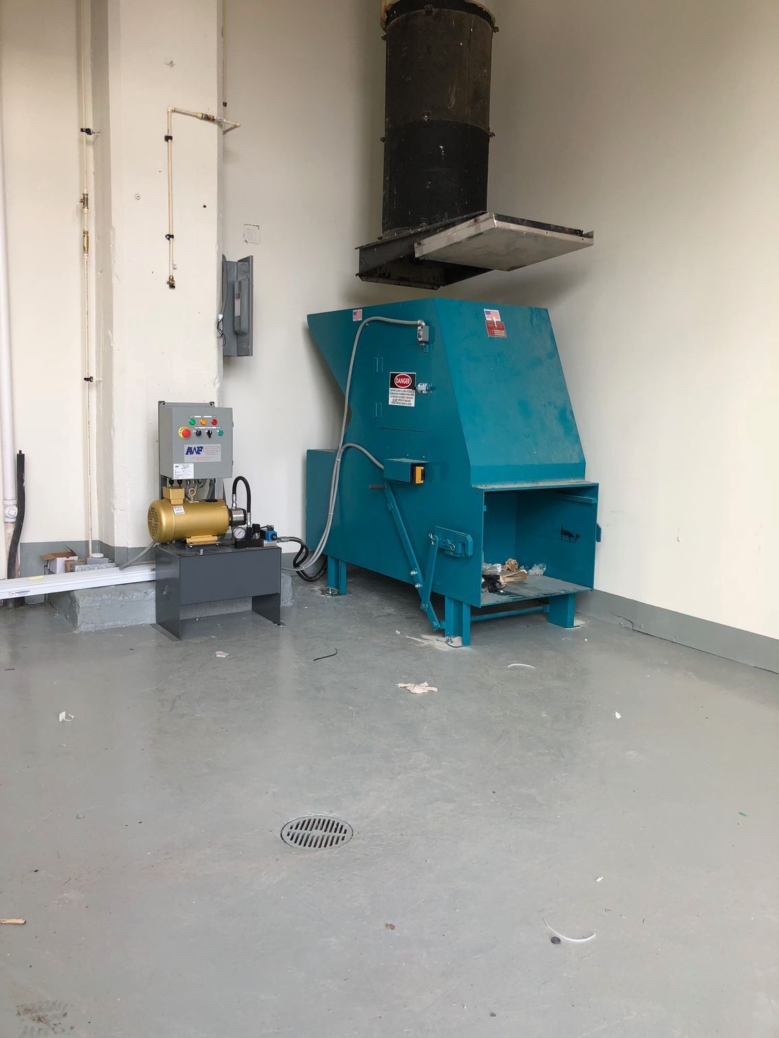 A large industrial shredder in a room, with a control panel and exhaust, and a shiny, gray floor.