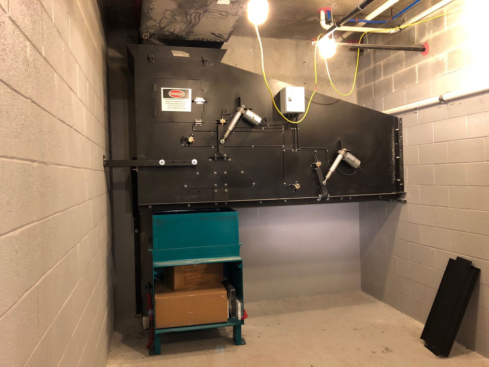 A large black HVAC unit mounted on a concrete wall in a utility room with storage and lighting.