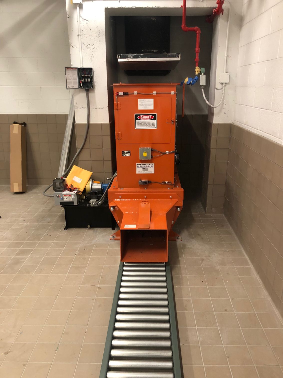 Orange industrial shredder with conveyor belt, inside a building.