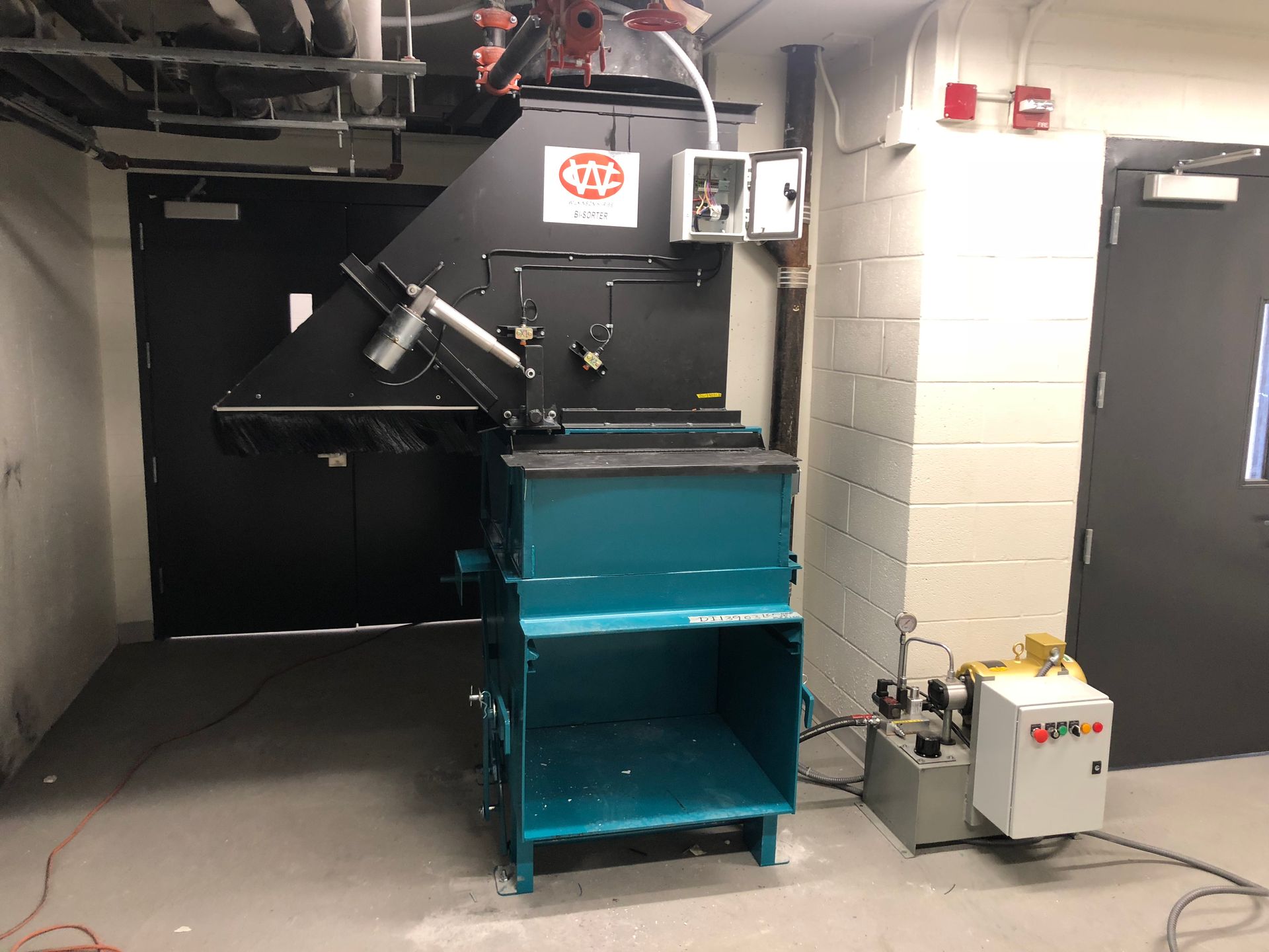 Blue and black industrial trash compactor in a utility room.