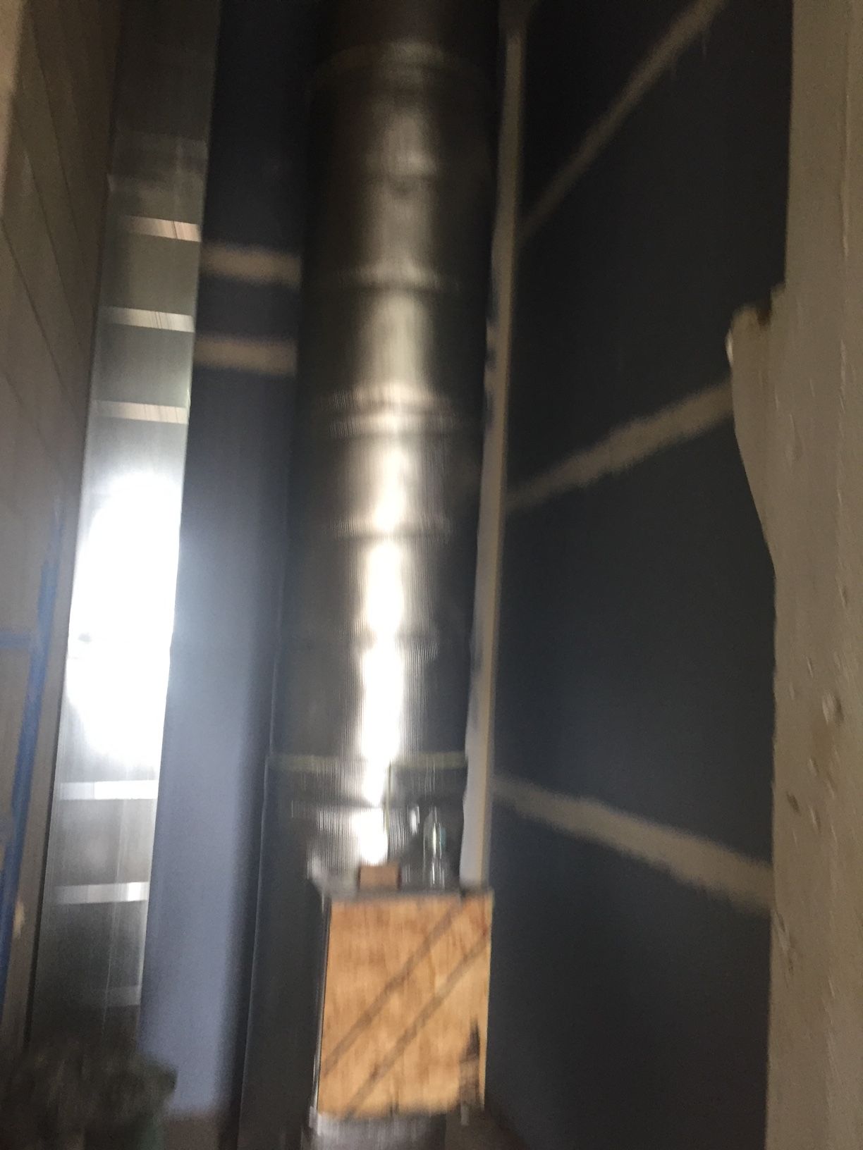 Metal ductwork and vent pipe in a narrow space between two walls.