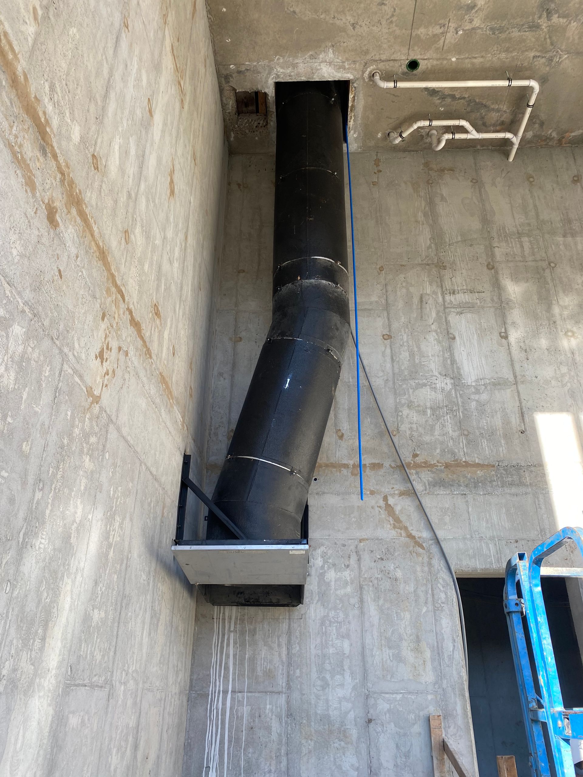 Black pipe angled through concrete wall. Blue cable and metal support visible.