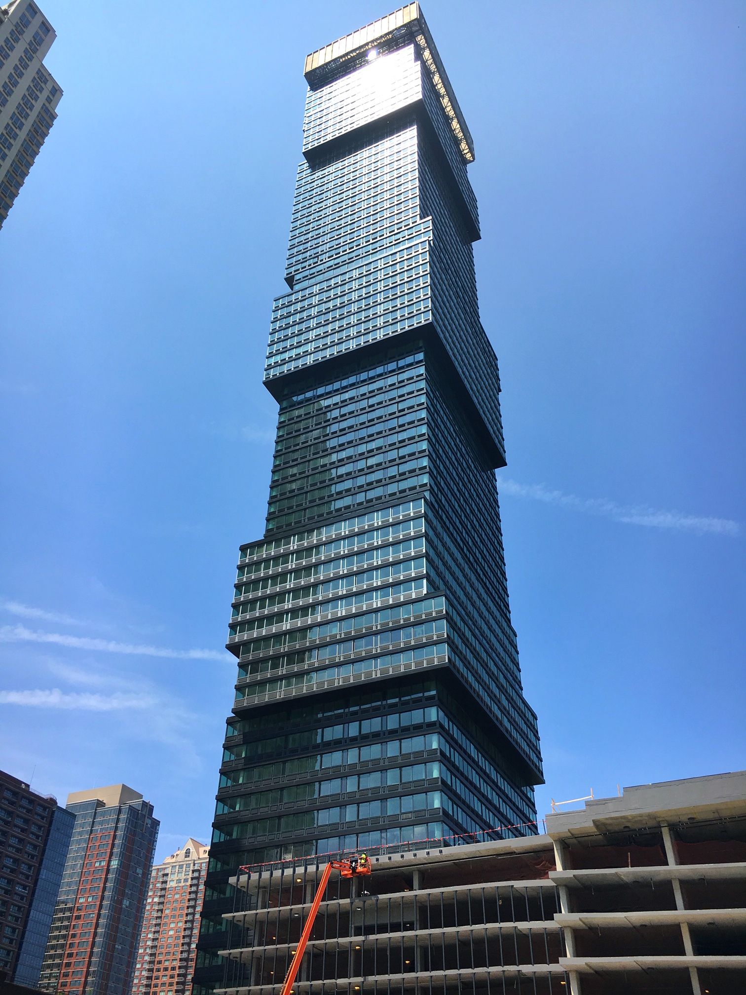 Tall modern skyscraper with blue glass facade against a bright sky.
