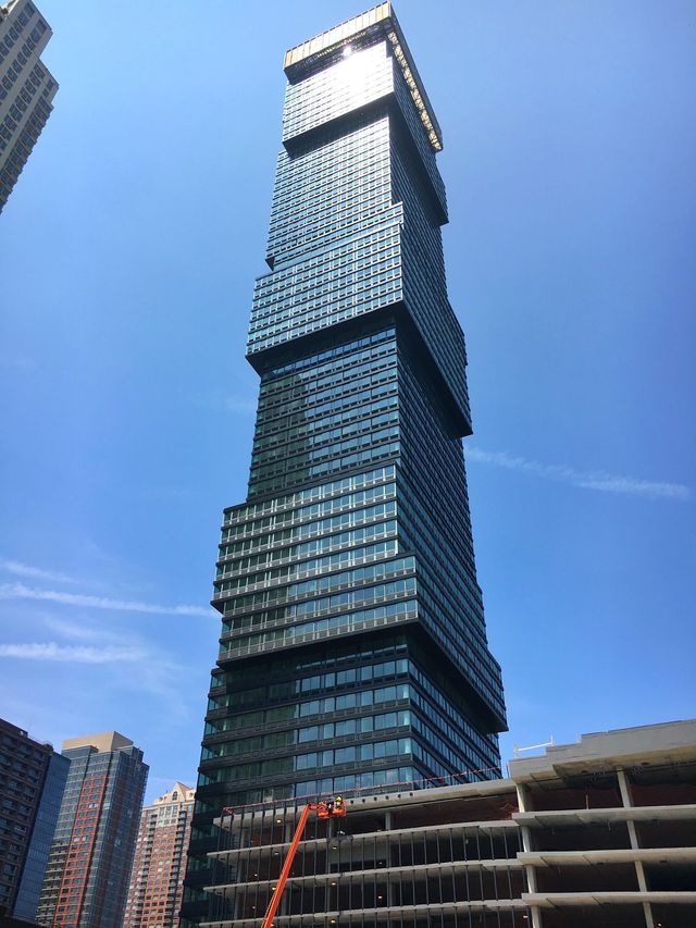 Tall, modern skyscraper with blue glass facade, against a clear blue sky.