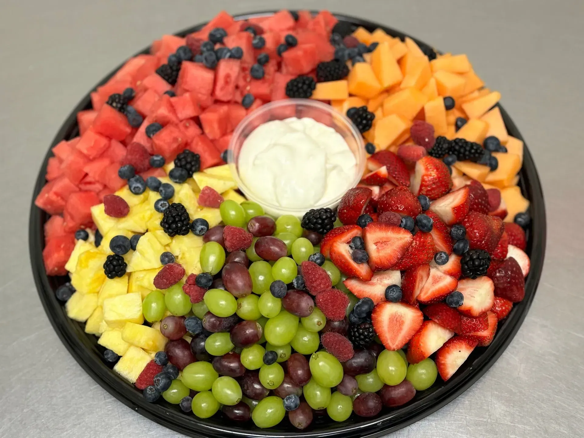 Fruit platter with watermelon, cantaloupe, strawberries, grapes, blueberries, and blackberries, with dip.
