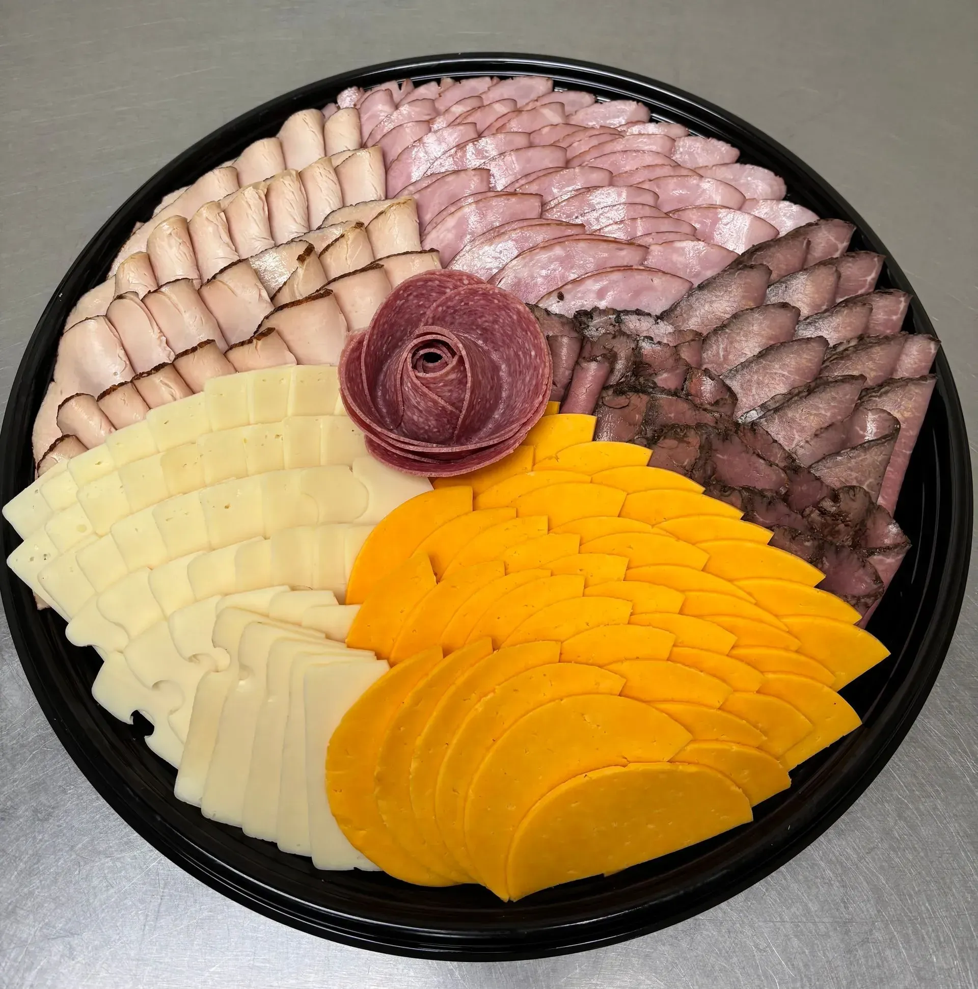 Charcuterie platter: meats, cheeses arranged in a circle, with a salami rose in the center.