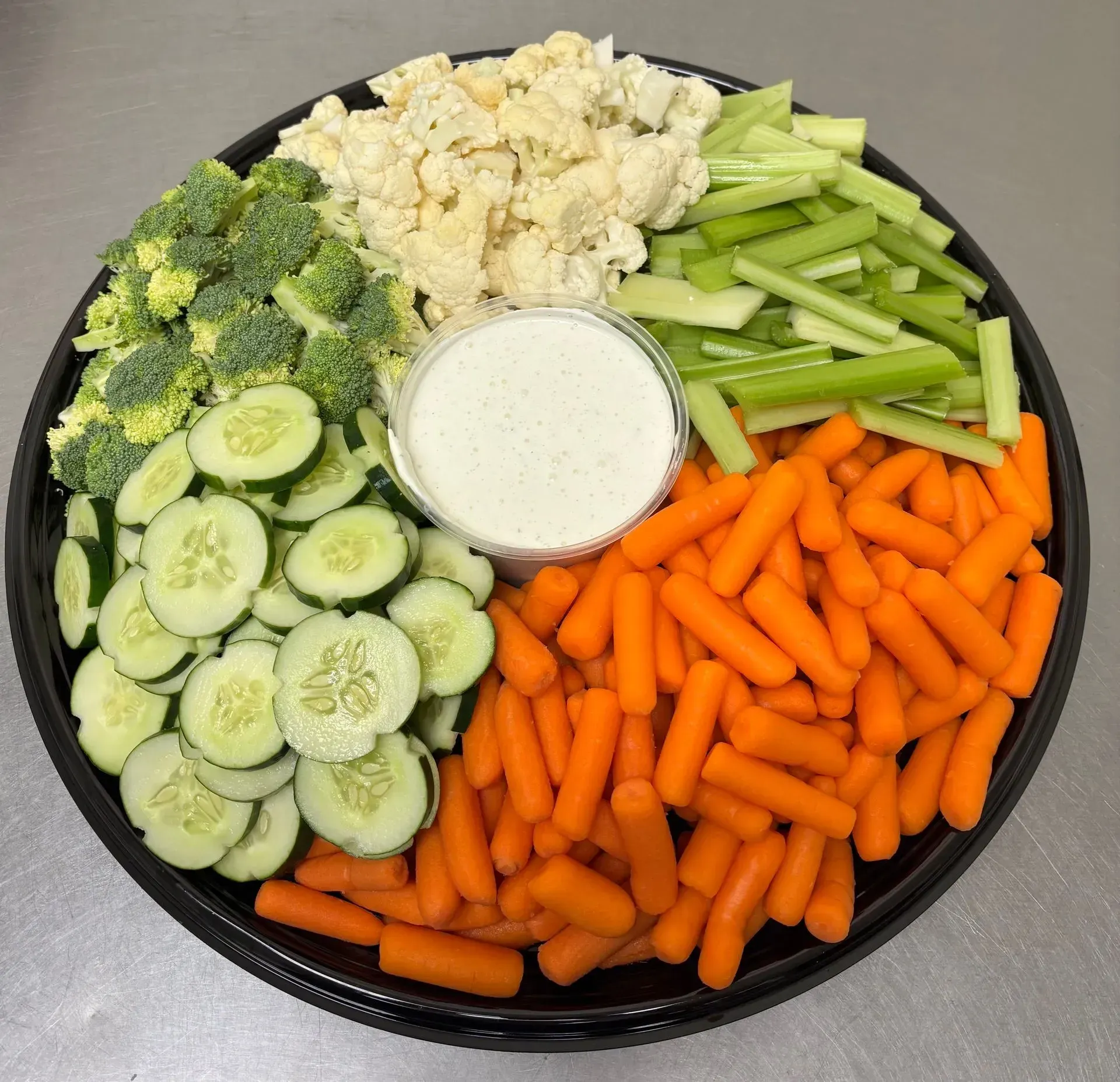 Vegetable platter with cucumbers, broccoli, cauliflower, celery, carrots, and dip.