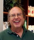 Smiling man in a green polo shirt standing in front of shelves in a shop or office