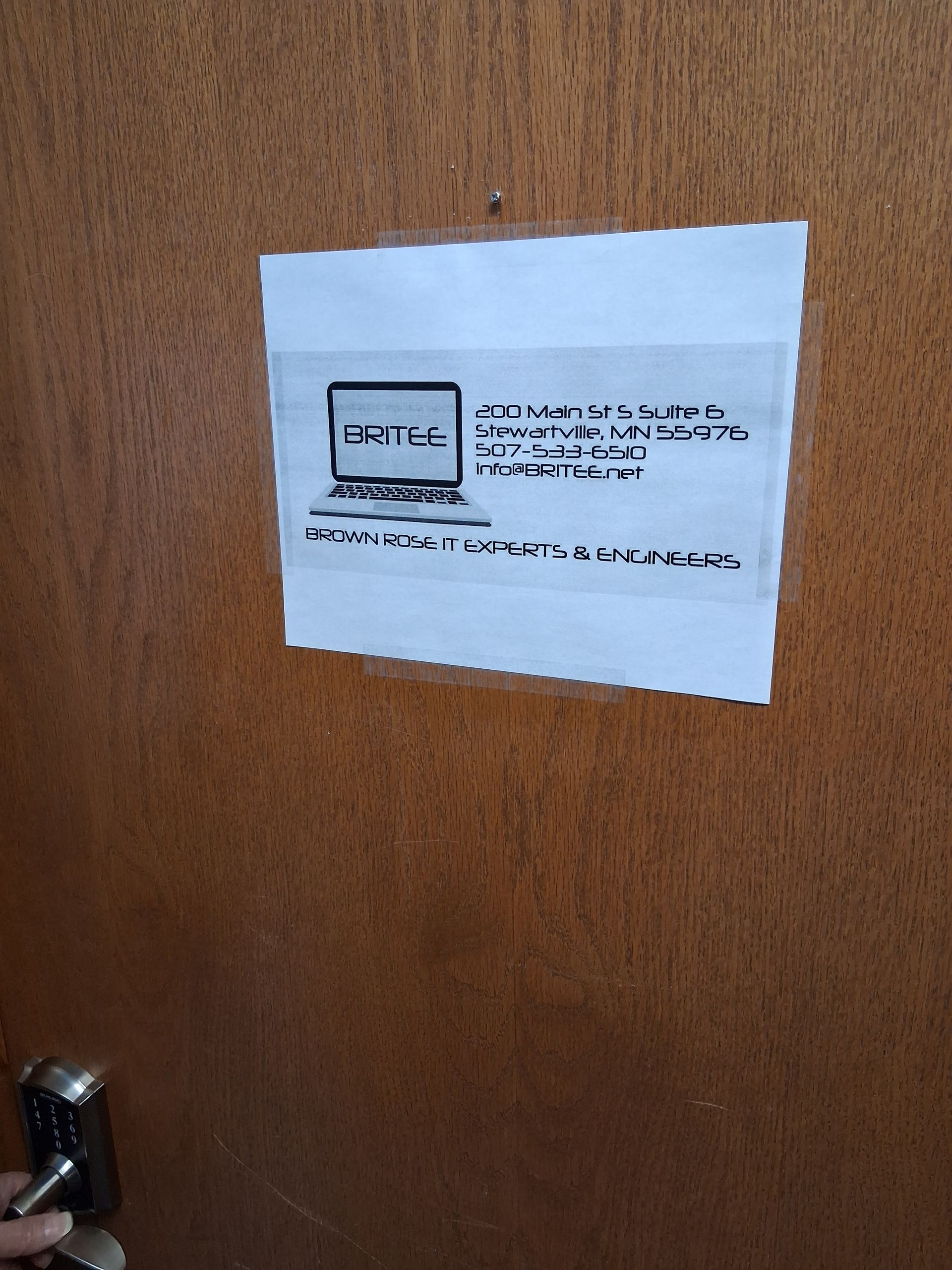 A sign taped to a wooden door featuring a computer icon and contact information for IT support services.