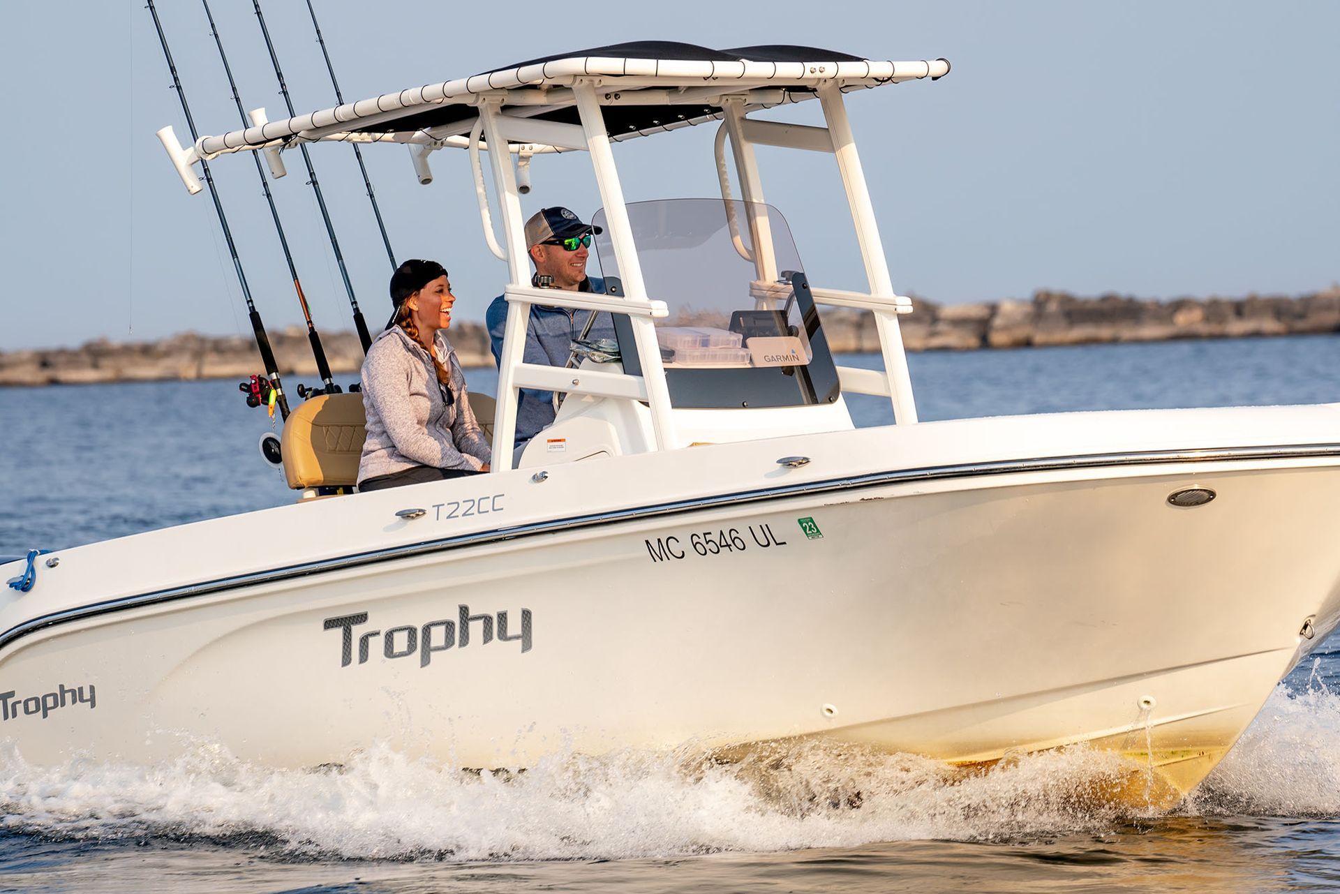 A white Trophy fishing boat with two people, driving on water.